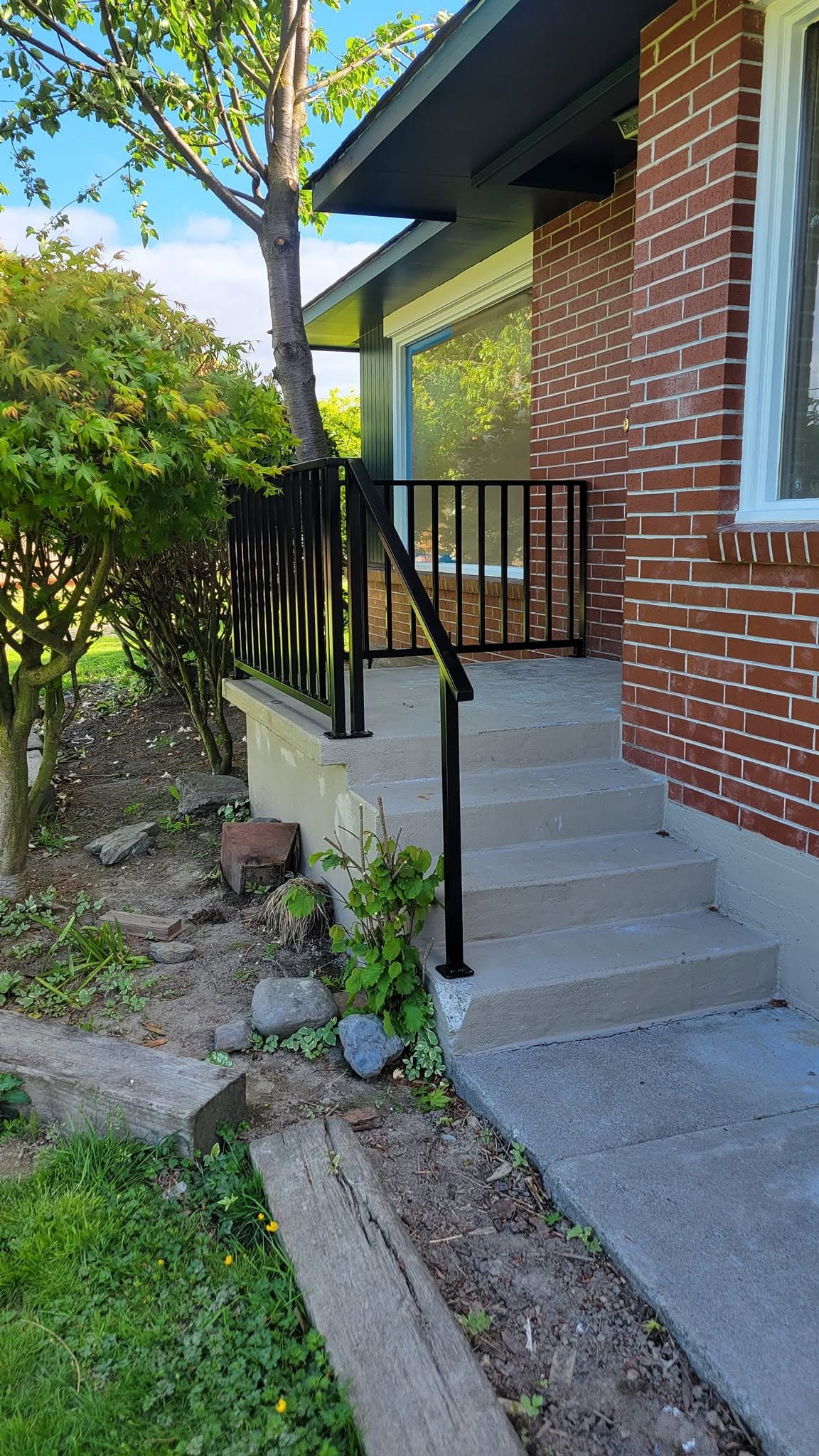 Custom-welded black metal handrail installed on residential exterior concrete steps.