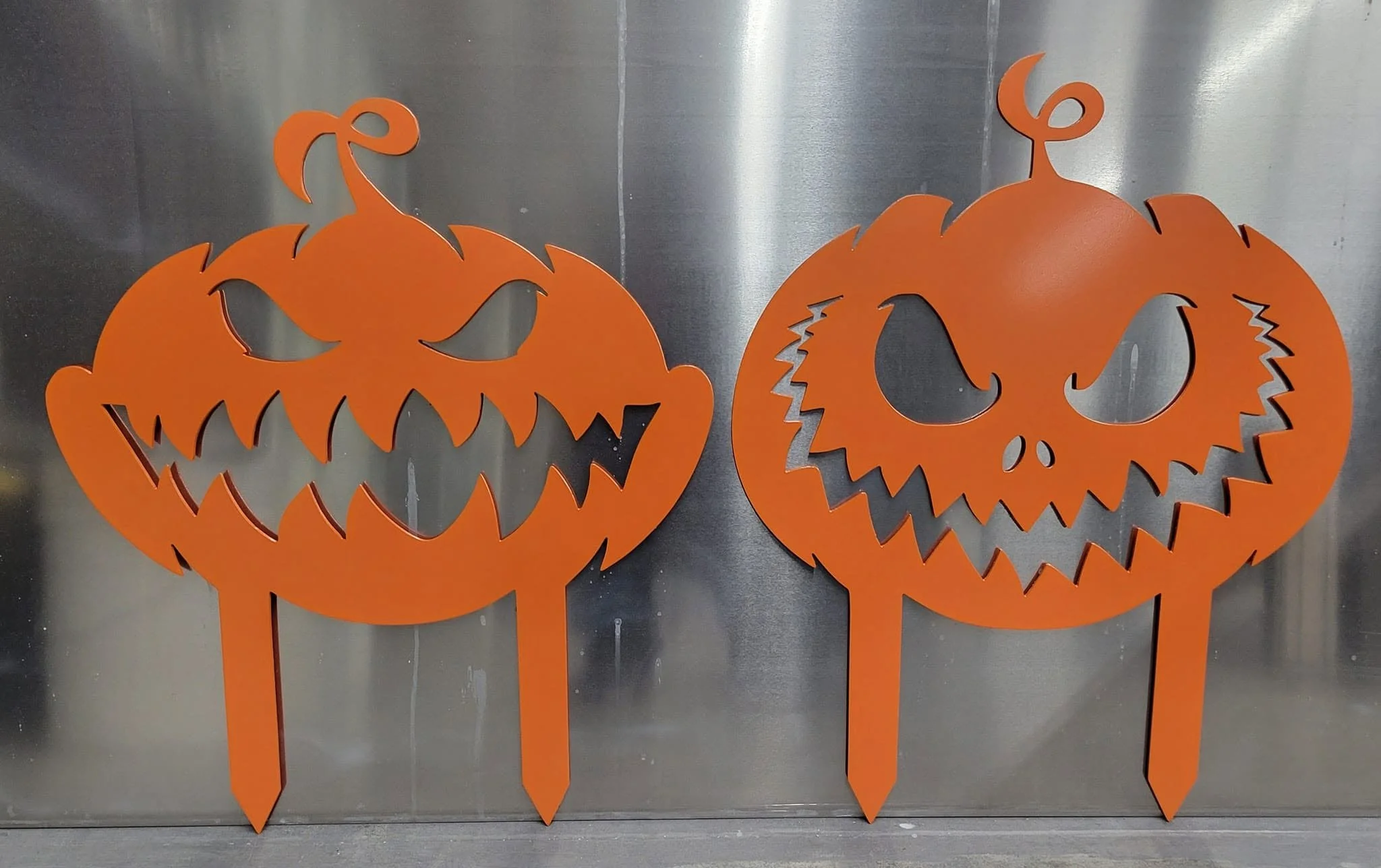 Set of custom CNC-cut metal jack-o'-lantern yard stakes with a vibrant orange powder-coated finish.