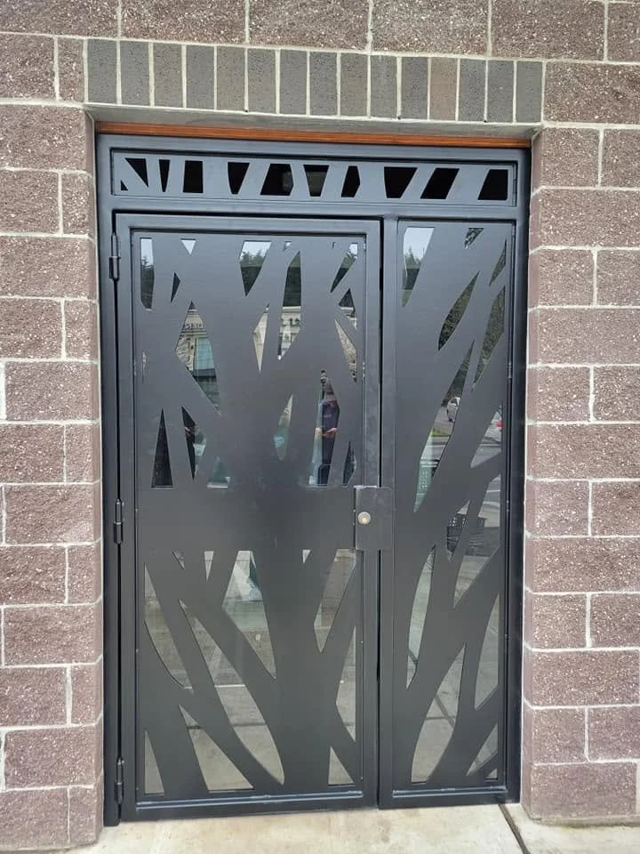 Modern black metal exterior door with a custom CNC-cut tree-branch aesthetic design.