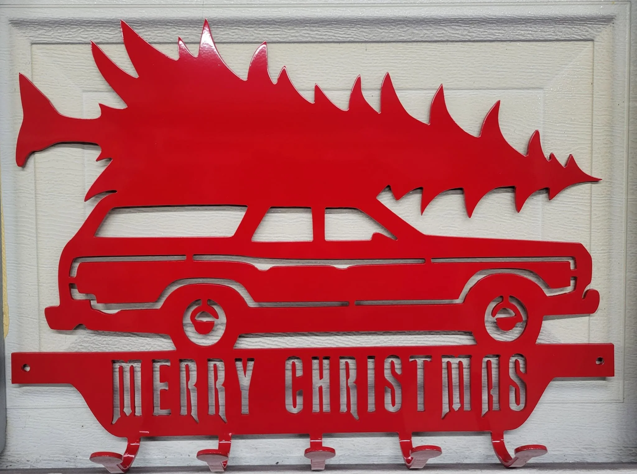 Custom-fabricated red metal Christmas holiday sign featuring a classic station wagon carrying a tree.