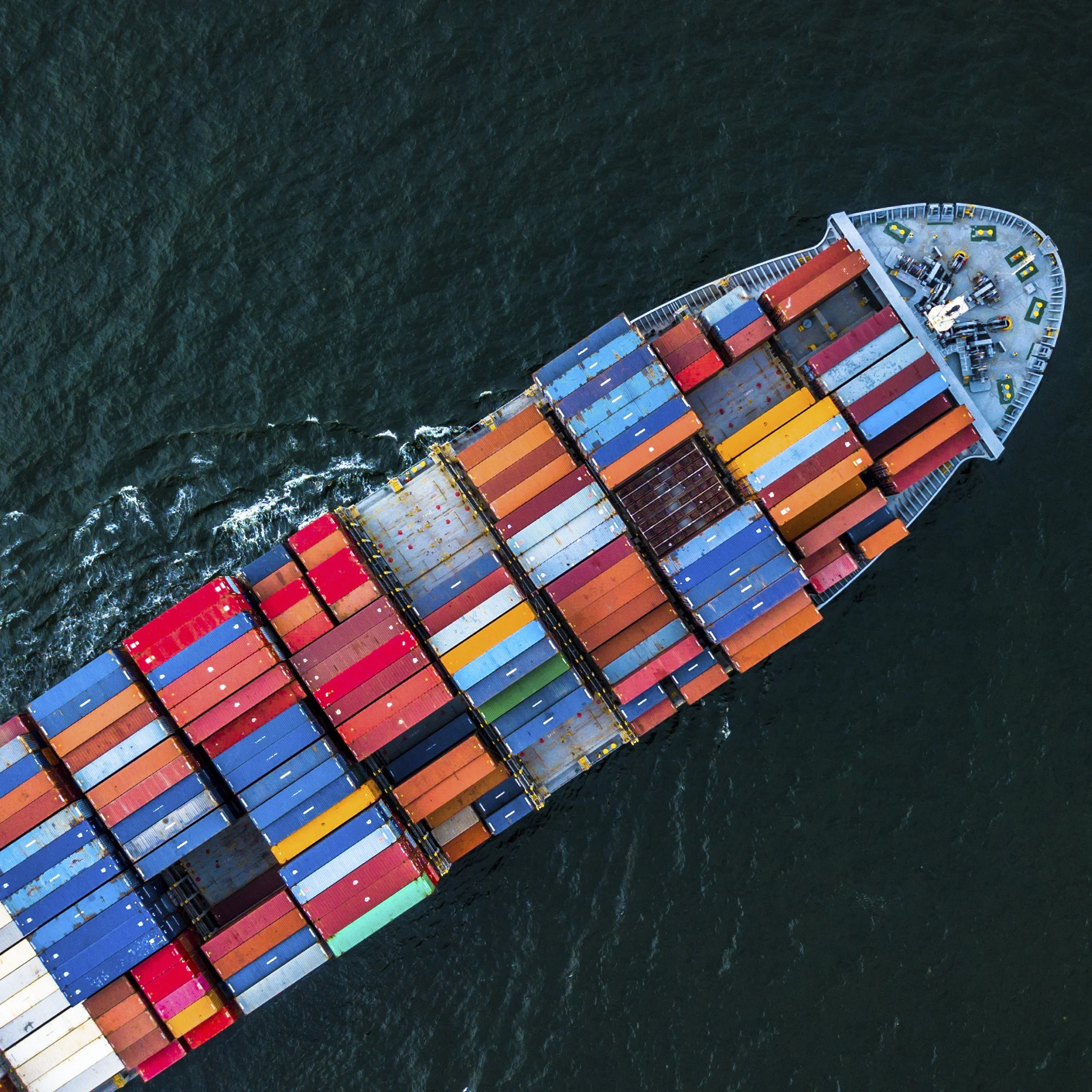 Aerial view of a large cargo ship sailing through the ocean carrying numerous colorful shipping containers.