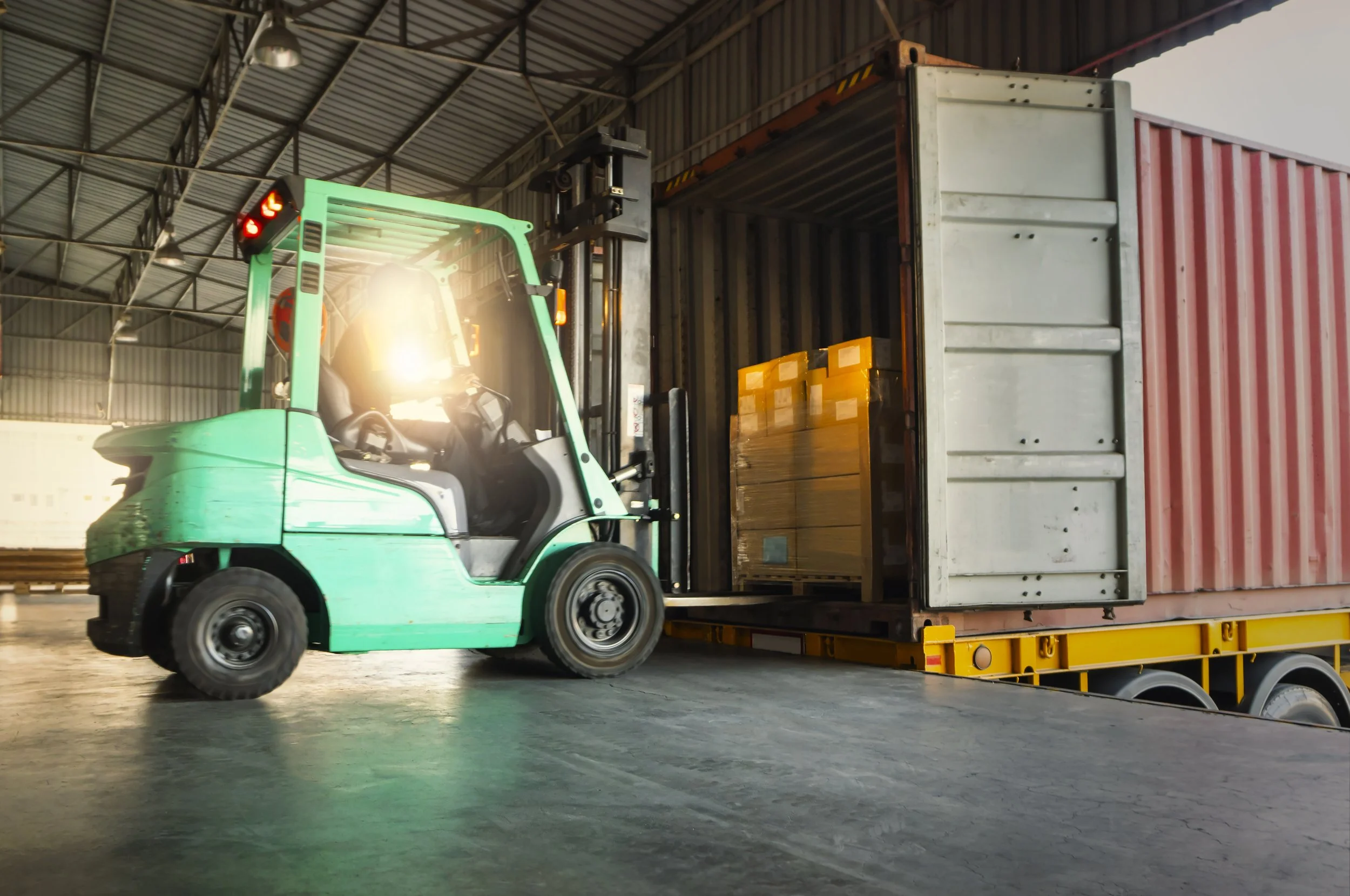 A forklift truck lifting a shipping container inside a warehouse.