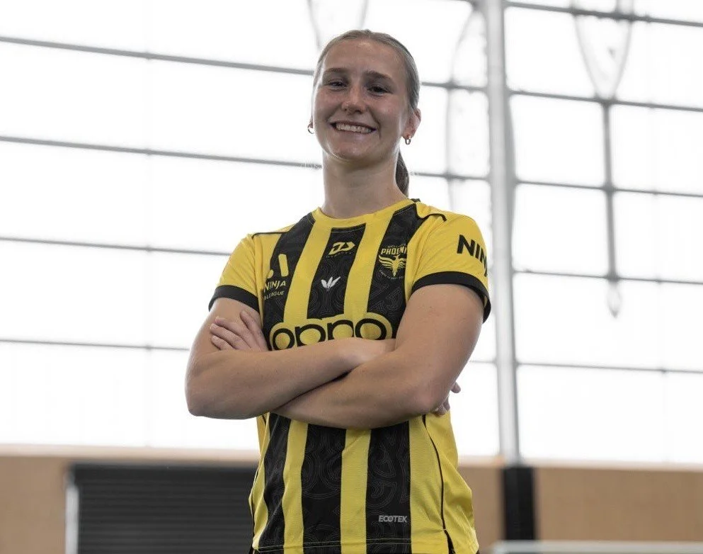 A young woman in a yellow and black sports jersey standing indoors with her arms crossed, smiling at the camera.