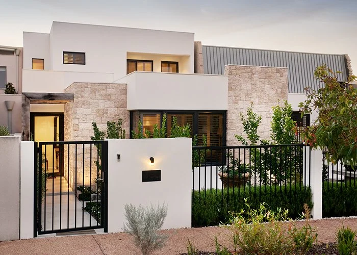 Modern residential home with white and stone exterior, black gate, and landscaped front yard with shrubs and trees.