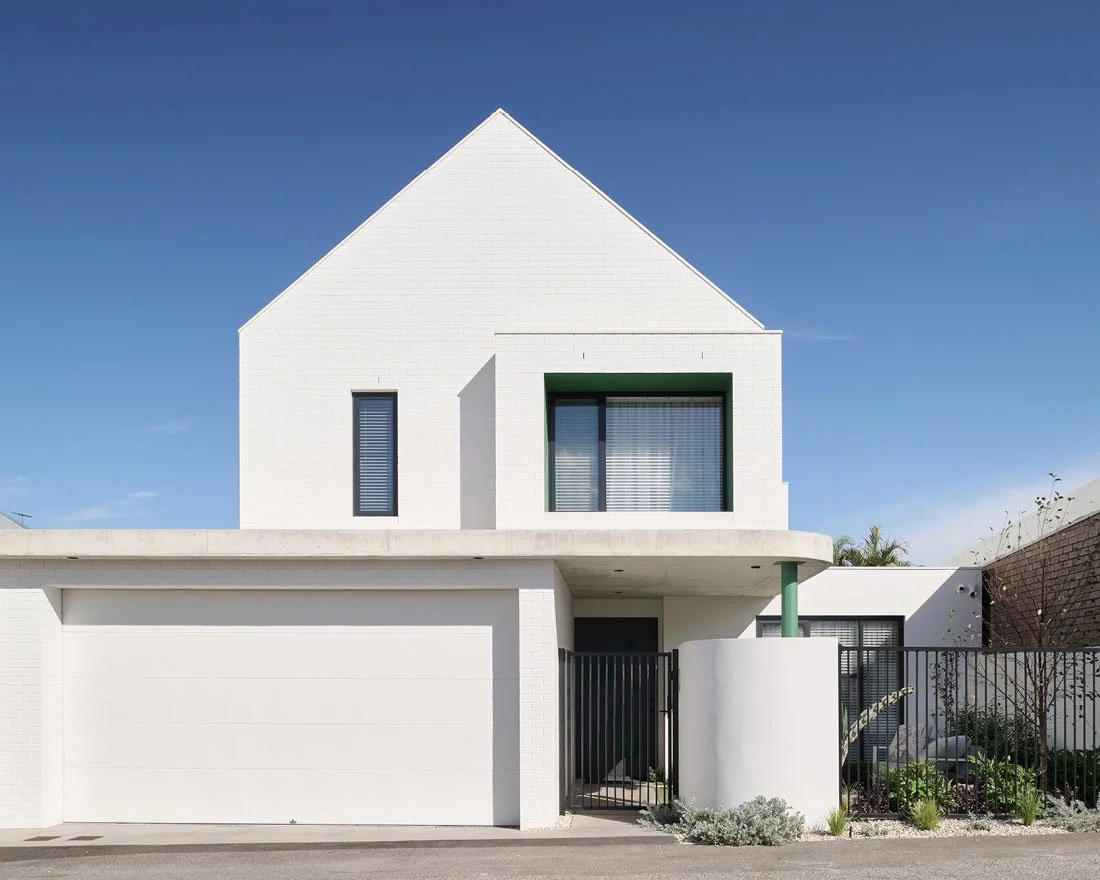 Modern white house with a gabled roof, black-framed windows, and a garage, with a small garden and a black gate in front.