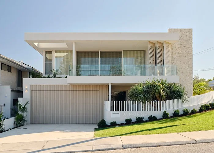 Modern two-story house with large windows, a garage, and landscaped front yard with shrubs and grass.