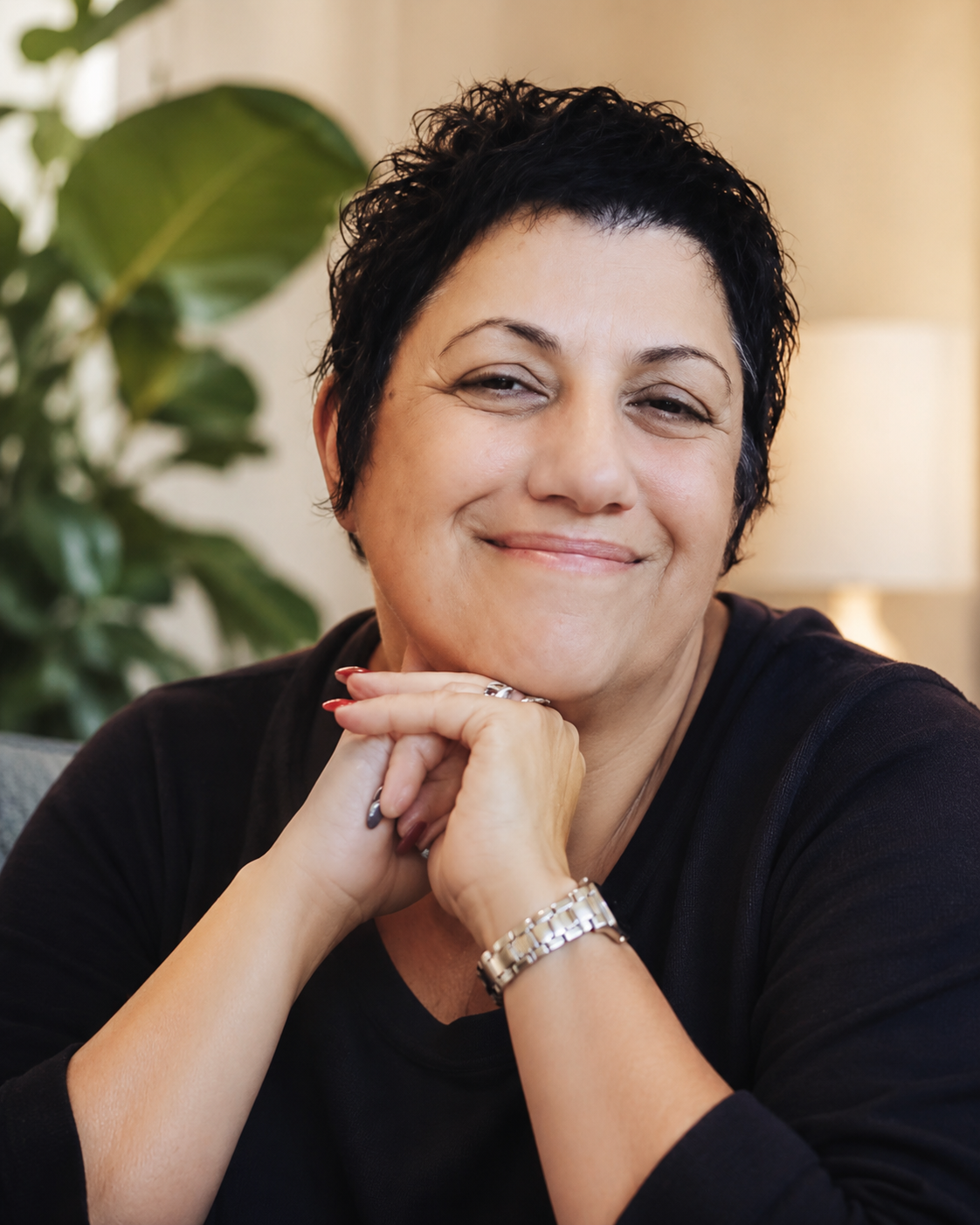 Smiling woman resting her chin on her hands in a calm indoor setting.