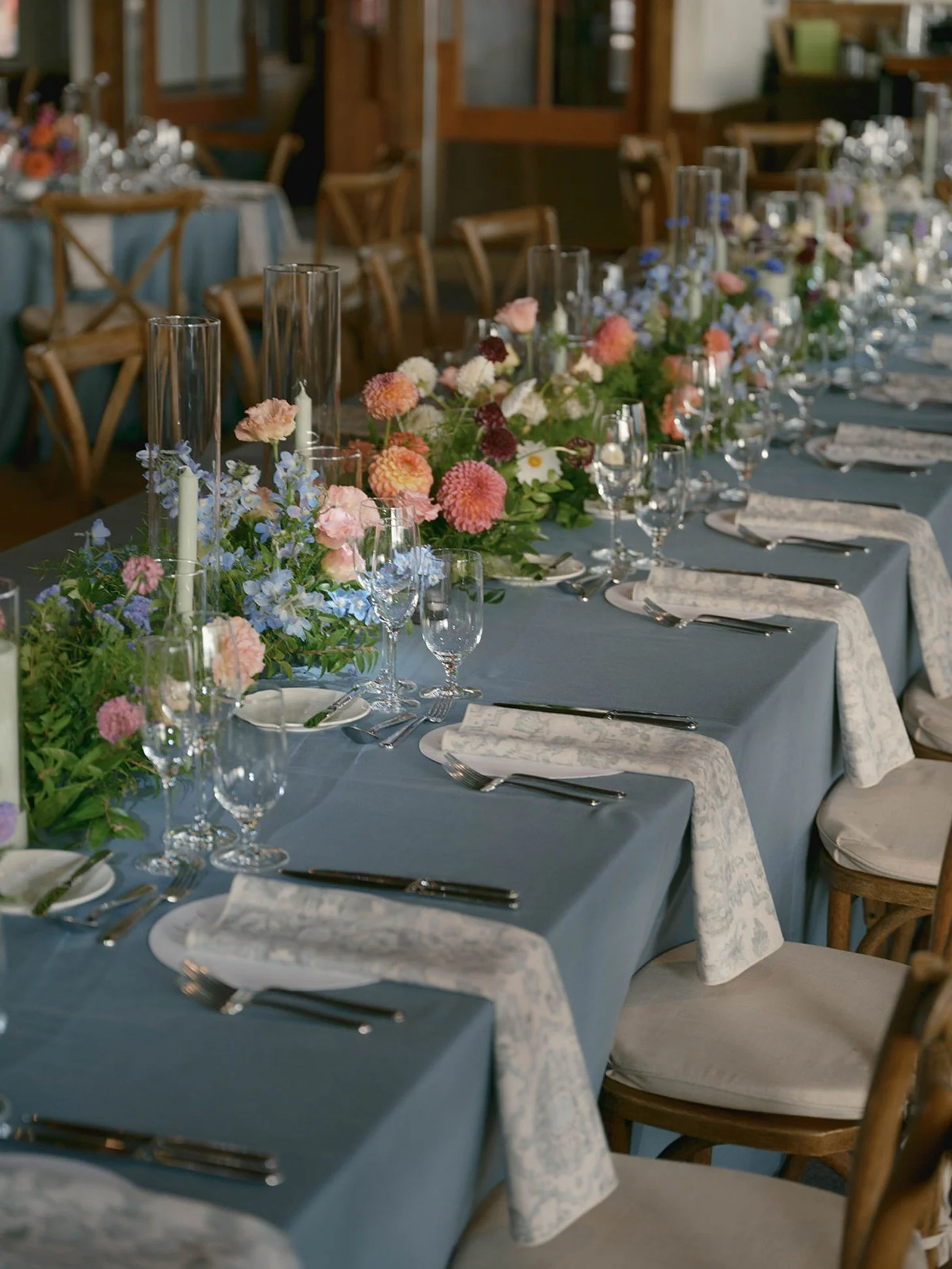 A long dining table decorated with a floral centerpiece and glassware in a rustic indoor setting.