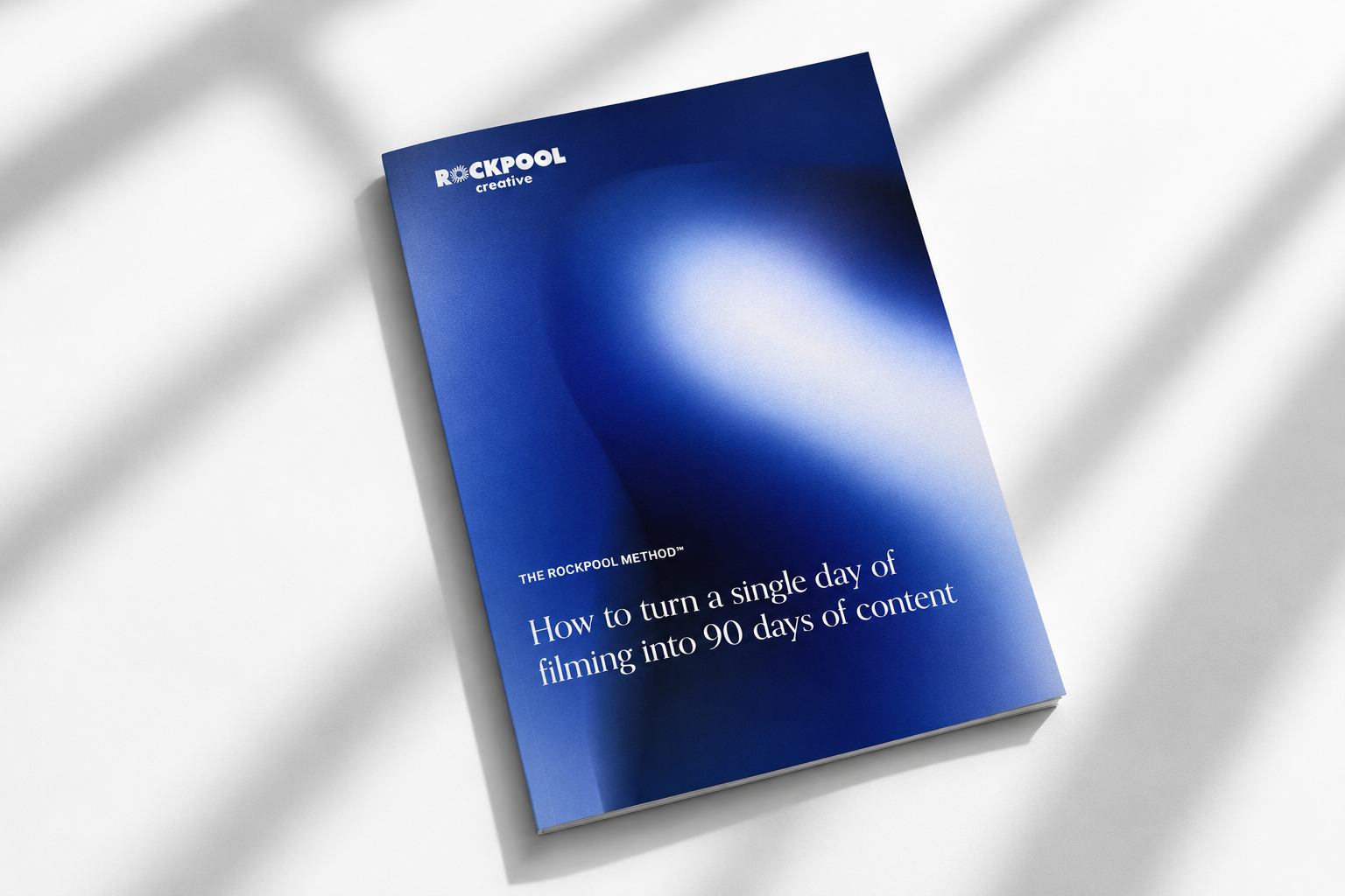 Blue digital guidebook titled 'The Rockpool Method: How to turn a single day of filming into 90 days of content' on a white surface with shadows.