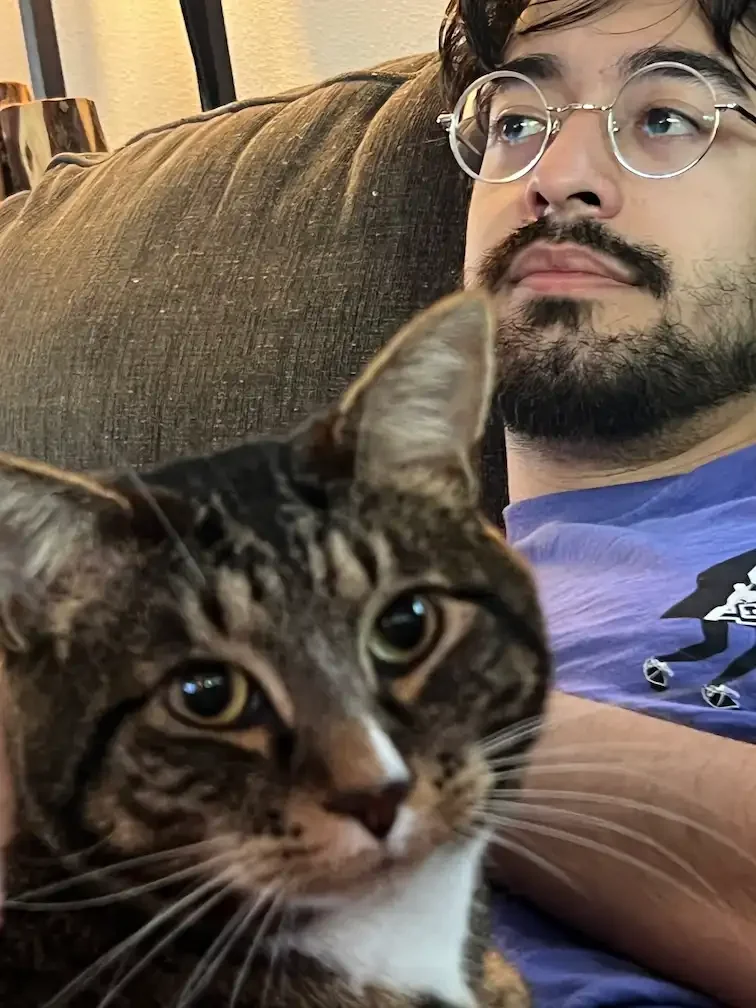 tafaar with his cat Poncho. Poncho is on tafaar's lap, looking at the camera while tafaar looks off to the side.