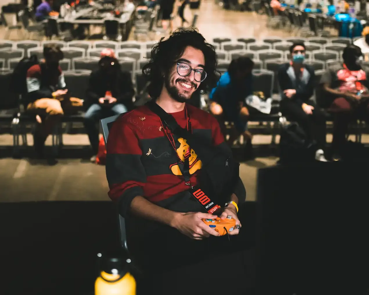 tafaar with shoulder-length hair and glasses smiling while holding an orange spice GameCube controller. He is sitting on-stage at Genesis 8 before a set against ThundeRzReiGN in Nickelodeon All-Star Brawl.