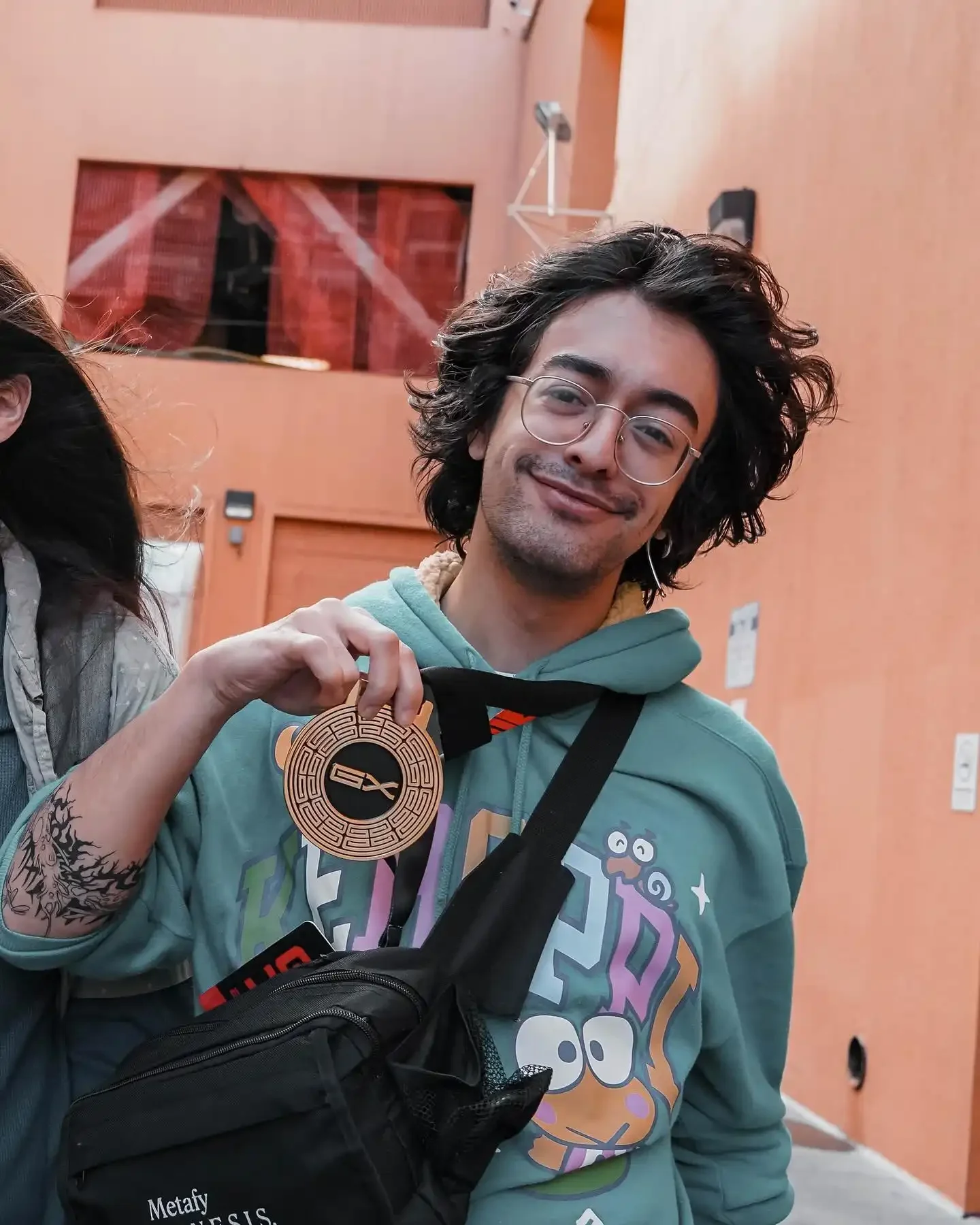 tafaar with glasses and shoulder-length curly hair holding a medal for placing 4th in Nickelodeon All-Star Brawl 2 at Genesis X. He is outside standing next to Rivals of Aether player Zeebee.