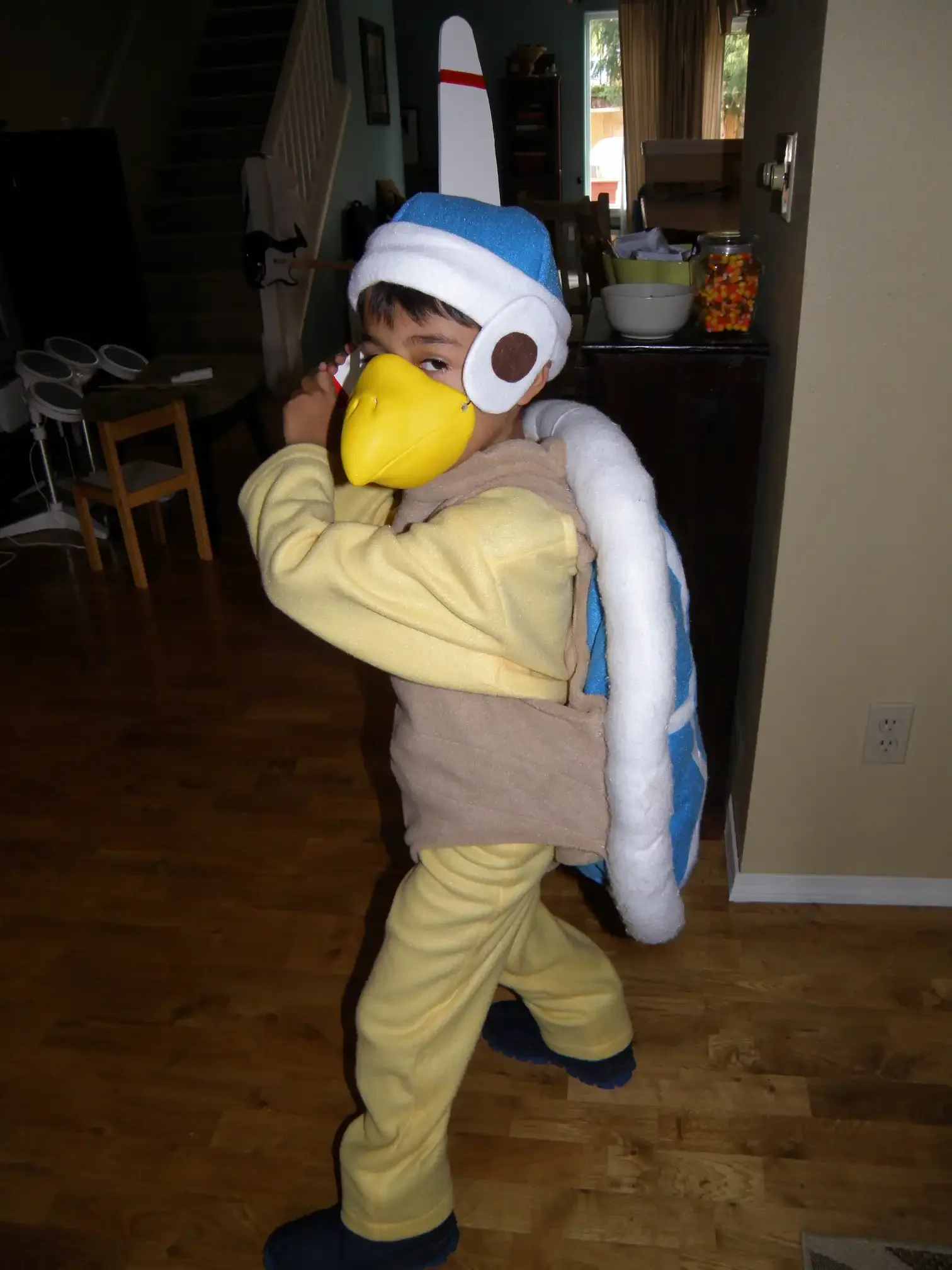 tafaar as a child dressed as a Boomerang Bro from Super Mario Bros for Halloween. He is in a battle-ready stance with the boomerang over his shoulder like a baseball bat. The room has hardwood flooring and beige walls.