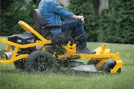 Person riding a yellow zero-turn riding lawn mower on grass.