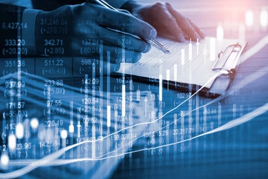 Hand holding a pen and writing on a notepad with financial charts and data overlays