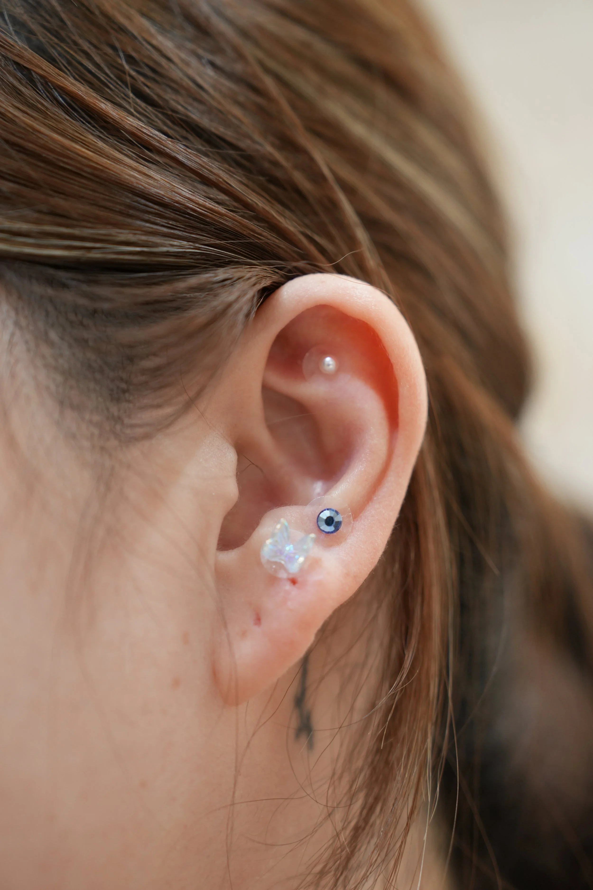 Close-up of a person's ear with a small pearl earring at the earlobe and a decorative butterfly-shaped earring, with brown hair partially covering the ear.