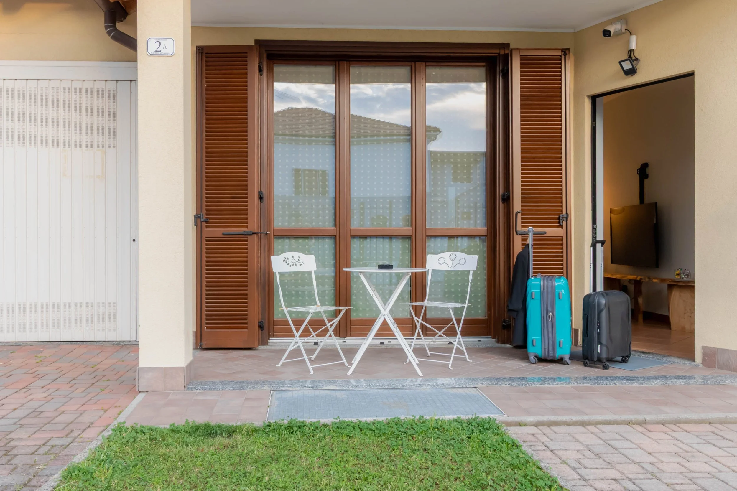 Balcone con tavolino e sedie bianco davanti a una finestra con persiane di legno, con valigie accanto.