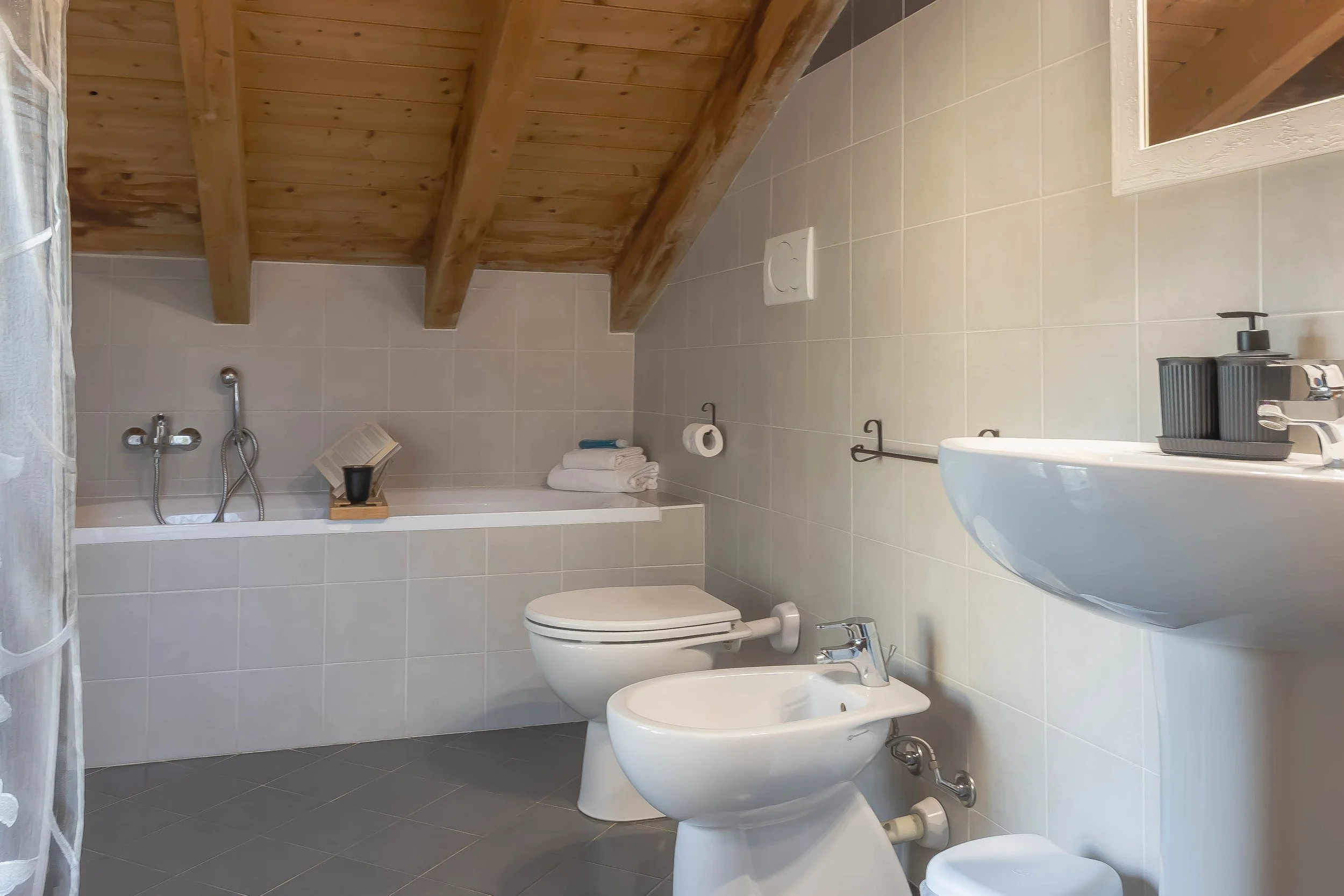 Bagno con soffitto in legno, lavabo con dispenser di sapone, gabinetto e bidet, specchio e accessori come porta rotolo e asciugamani MXP | Cardano al Campo | Cascina Costa | Gallarate | RaDa Homes di Daniela Raparoli 