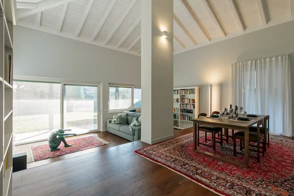 Interno di una casa con zona soggiorno e zona pranzo, con soffitti a volta in legno e grandi finestre.