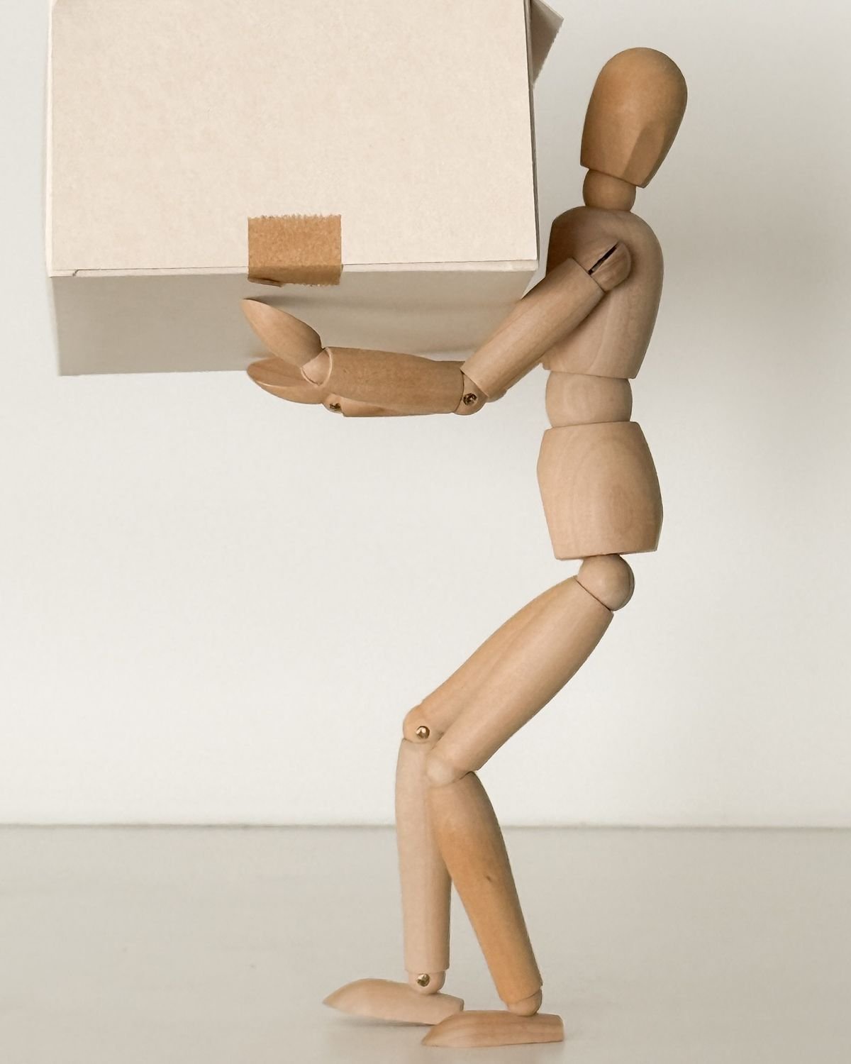 Una figura di legno a forma di manichino sta in piedi e tiene una scatola di cartone con nastro adesivo sulla parte superiore.