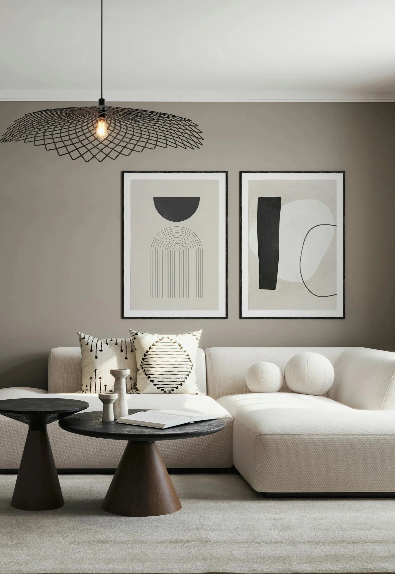 A modern living room with a white sofa, black and white abstract art on the wall, a black metal pendant light, and three white spherical decorative objects. Two black wooden tables with candles and a book are in the foreground.