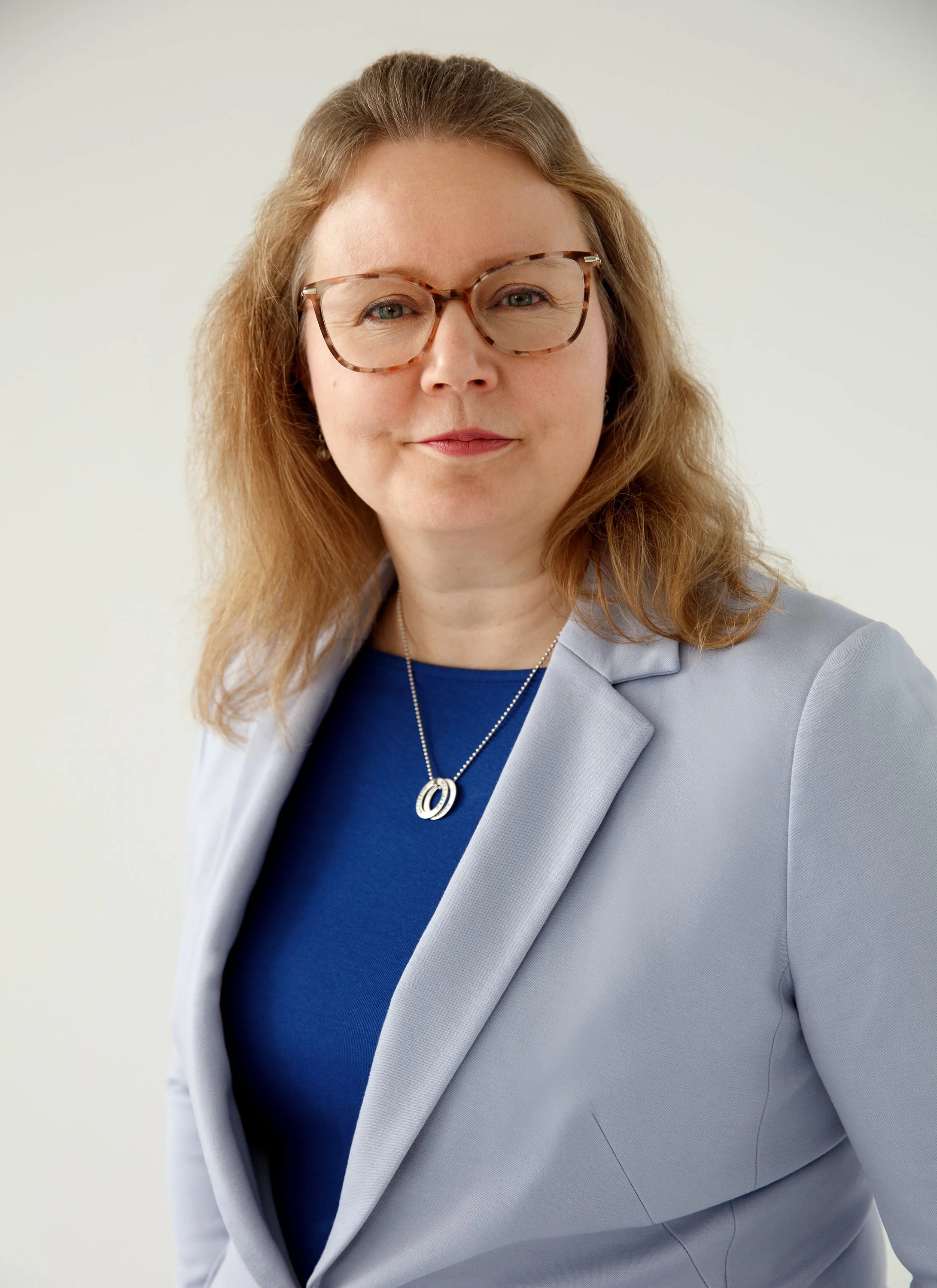 Kuvassa on Kristiina joka toimii TYYNI Remontit & Huollot Oy:ssä asiakkuus- ja hallintovastaavana. Kuva on otettu studiossa ja Kristiinalla on päällään vaaleansininen bleiseri.