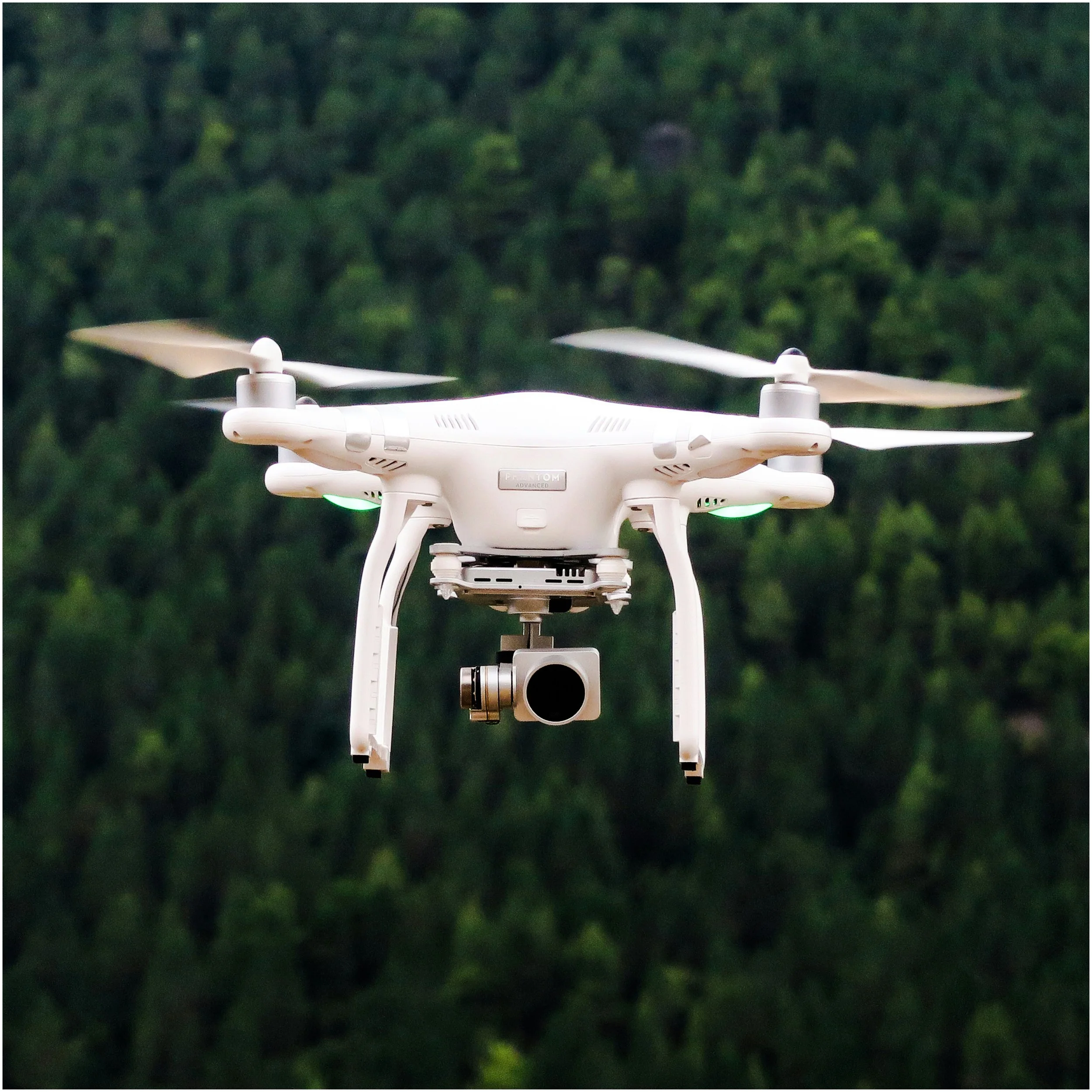 A white quadcopter drone flying outdoors with a background of green trees.
