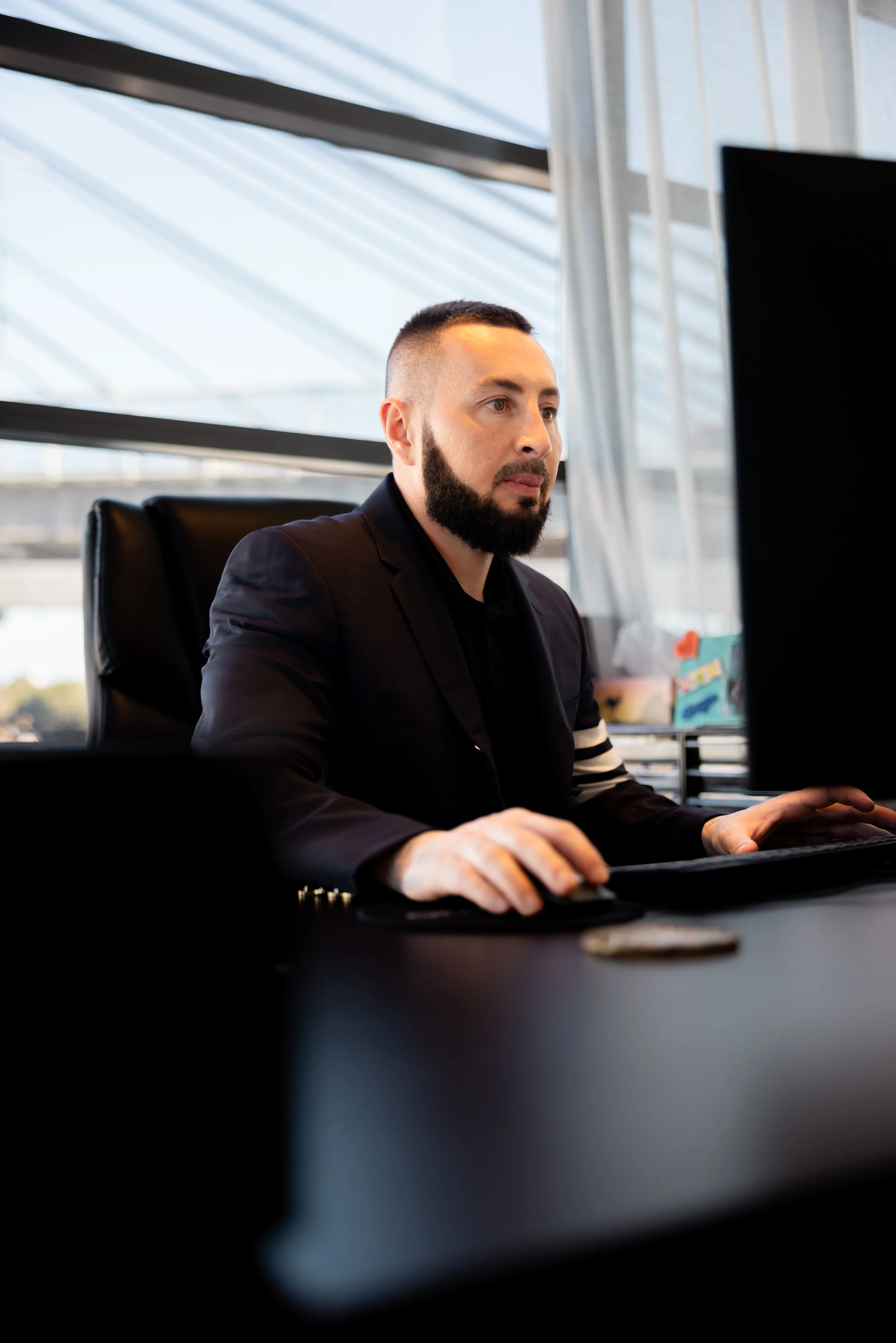 A man working at a desk in an office with large windows and blue sky outside.