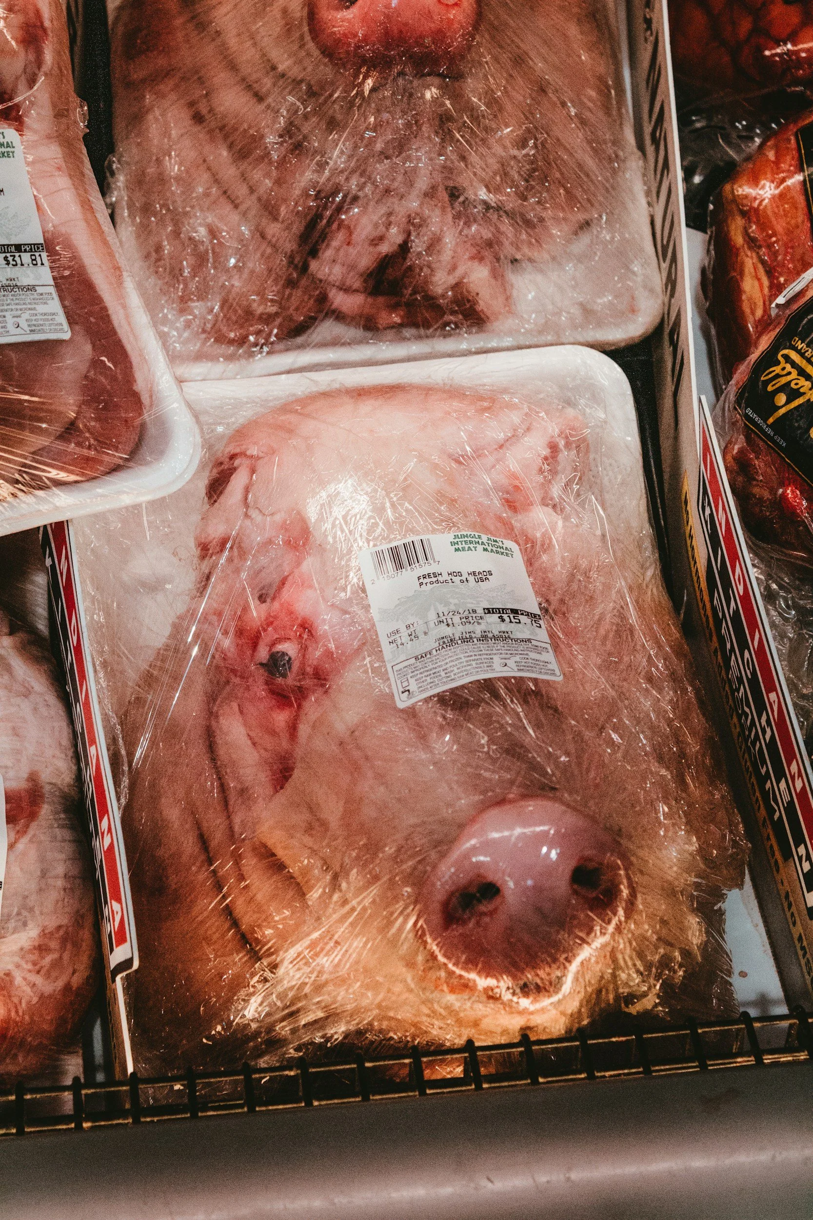 A fresh pig's head wrapped in plastic in a grocery store display.