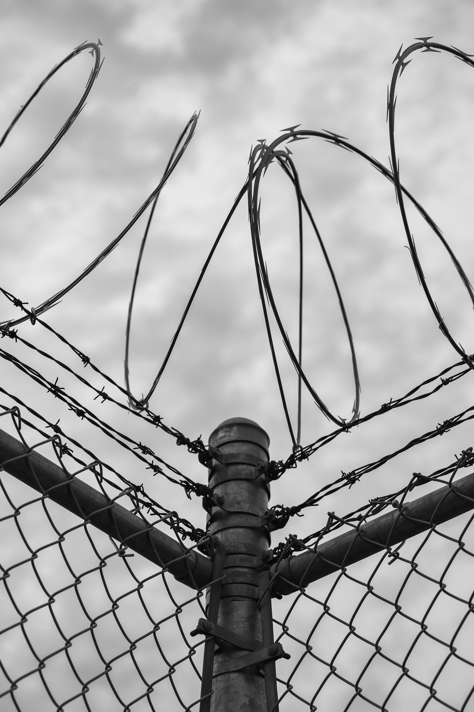 Barbed wire fence with a chain-link fence in the foreground and cloudy sky in the background.