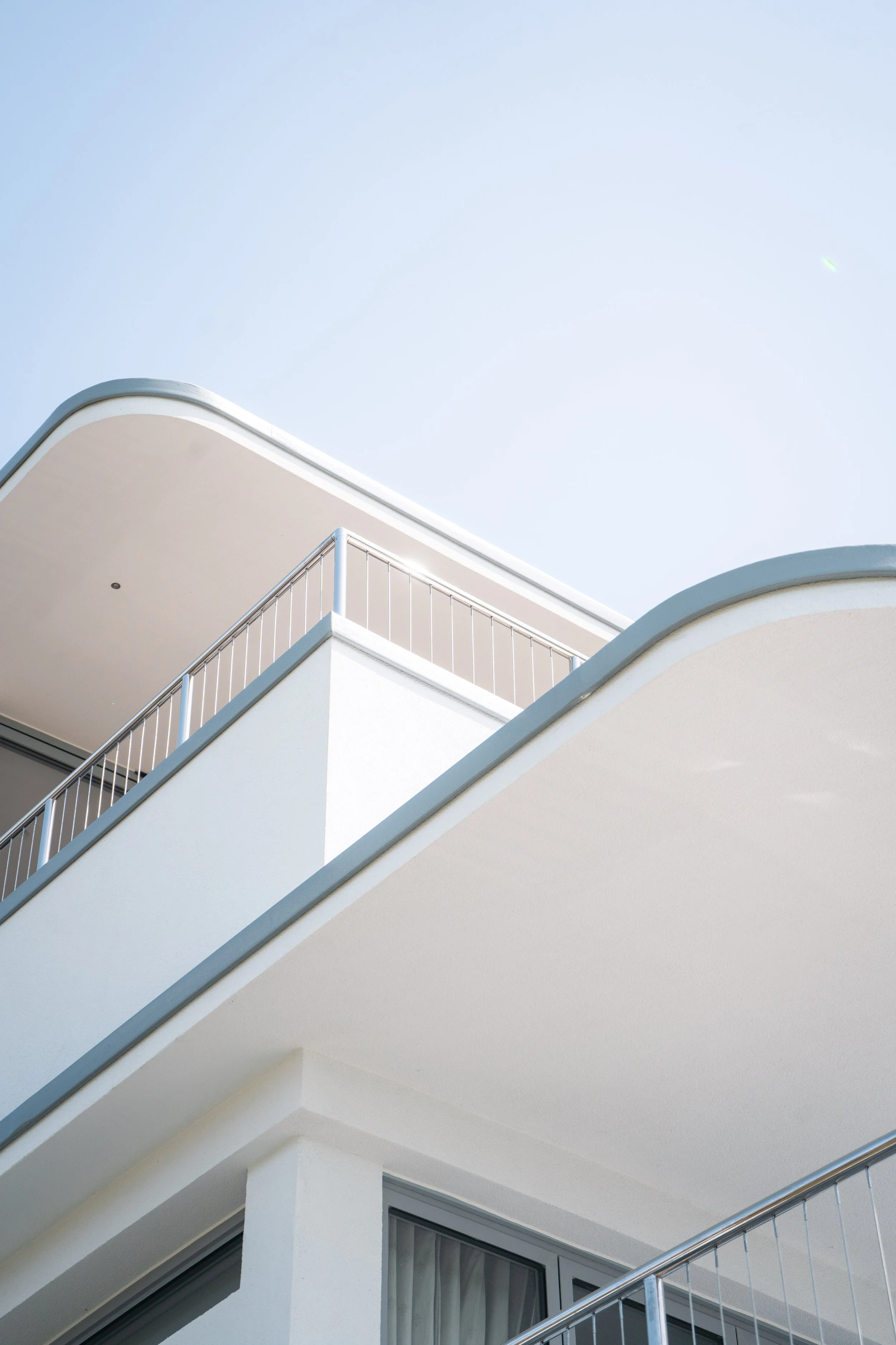 Close-up of a modern white building with curved balconies and silver railings against a clear blue sky.