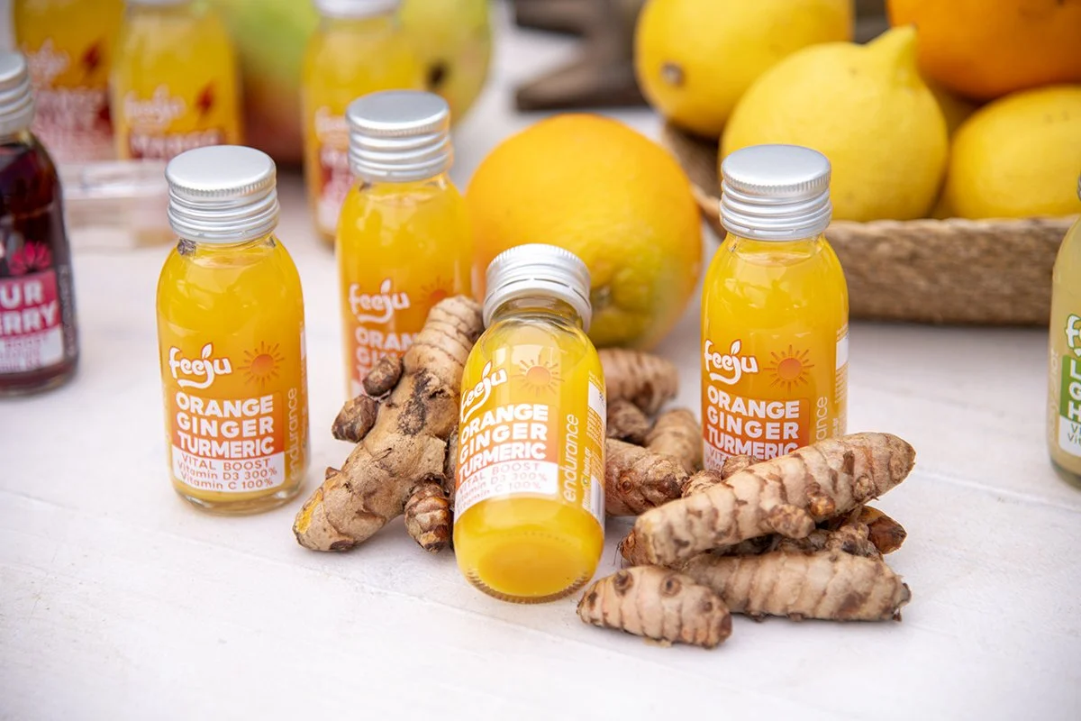 Bottles of orange ginger turmeric supplement with ginger roots and lemons on a white surface.
