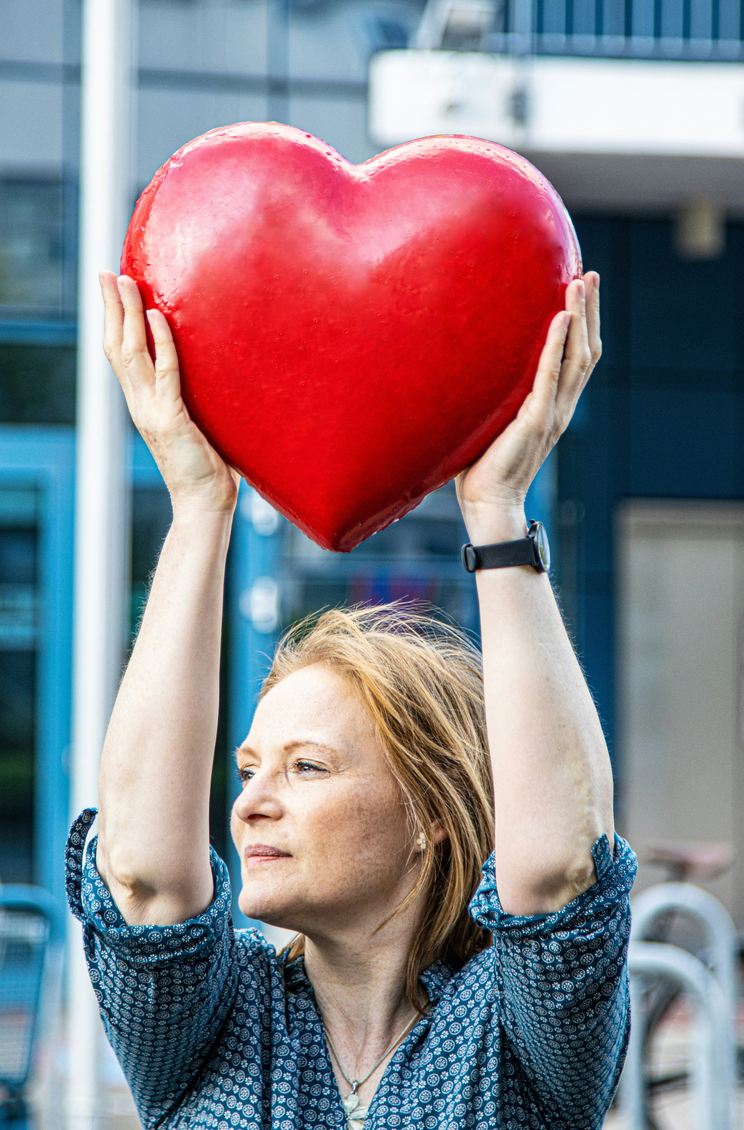 Photo by Marek Studzinski on Unsplash - a women holding a big red heart above her head