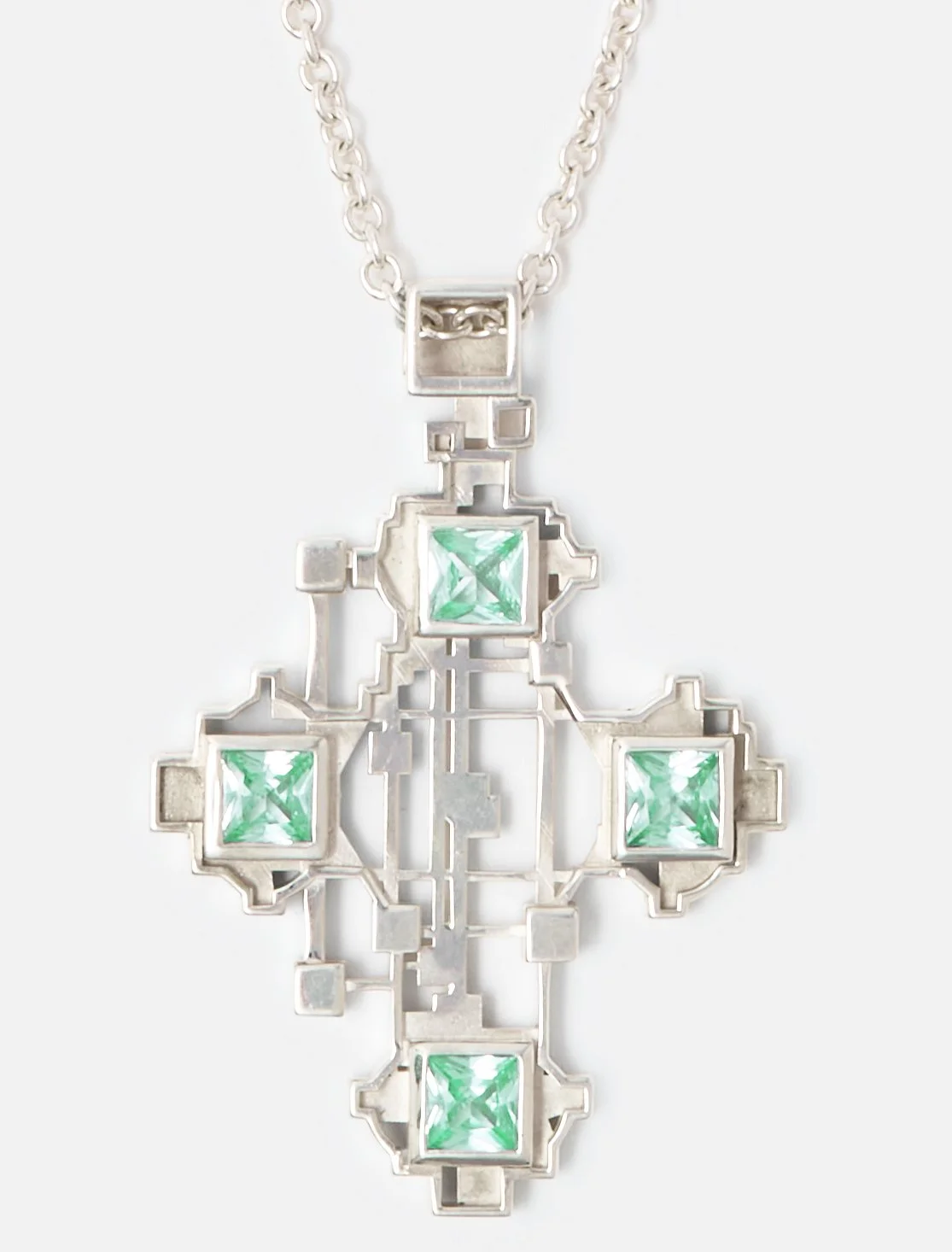 Silver necklace with geometric pendant featuring green square gemstones arranged in a cross pattern.