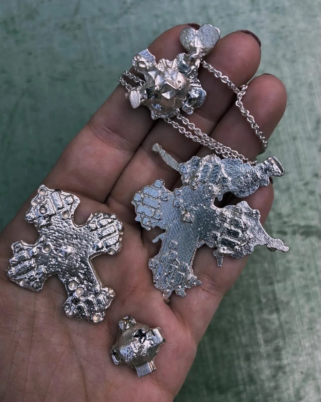 Hand holding multiple silver jewelry pieces with abstract and textured designs.