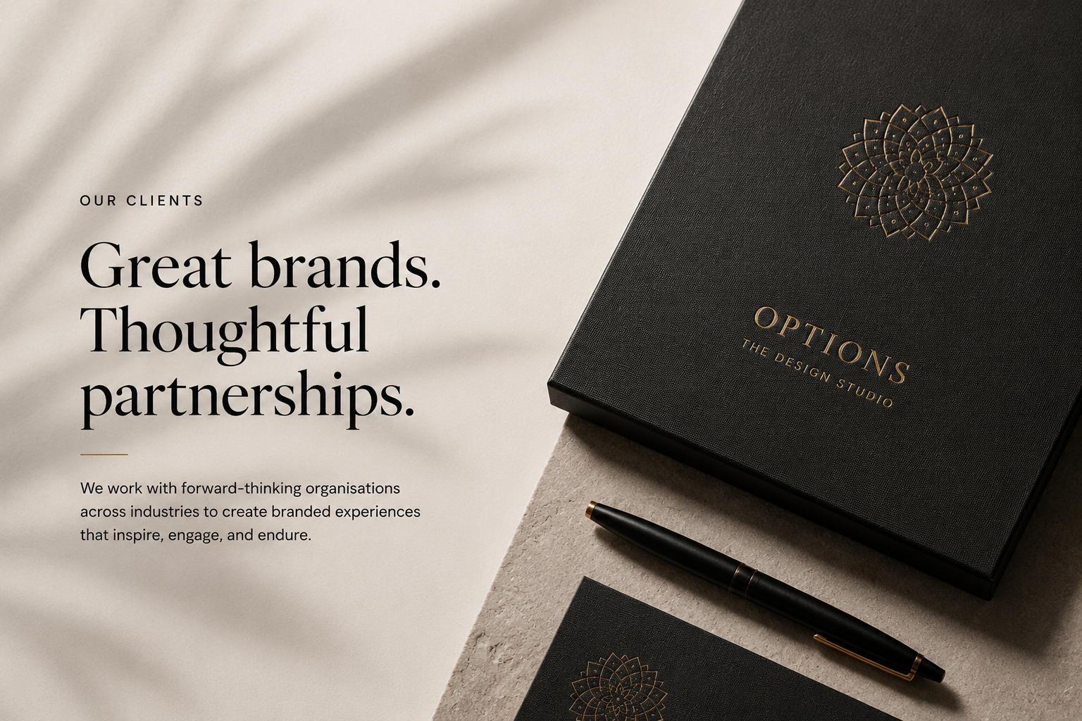 A black box with gold embossed logo and text reading 'OPTIONS THE DESIGN STUDIO' placed on a beige textured surface along with a black pen and a booklet featuring similar gold embossed design.