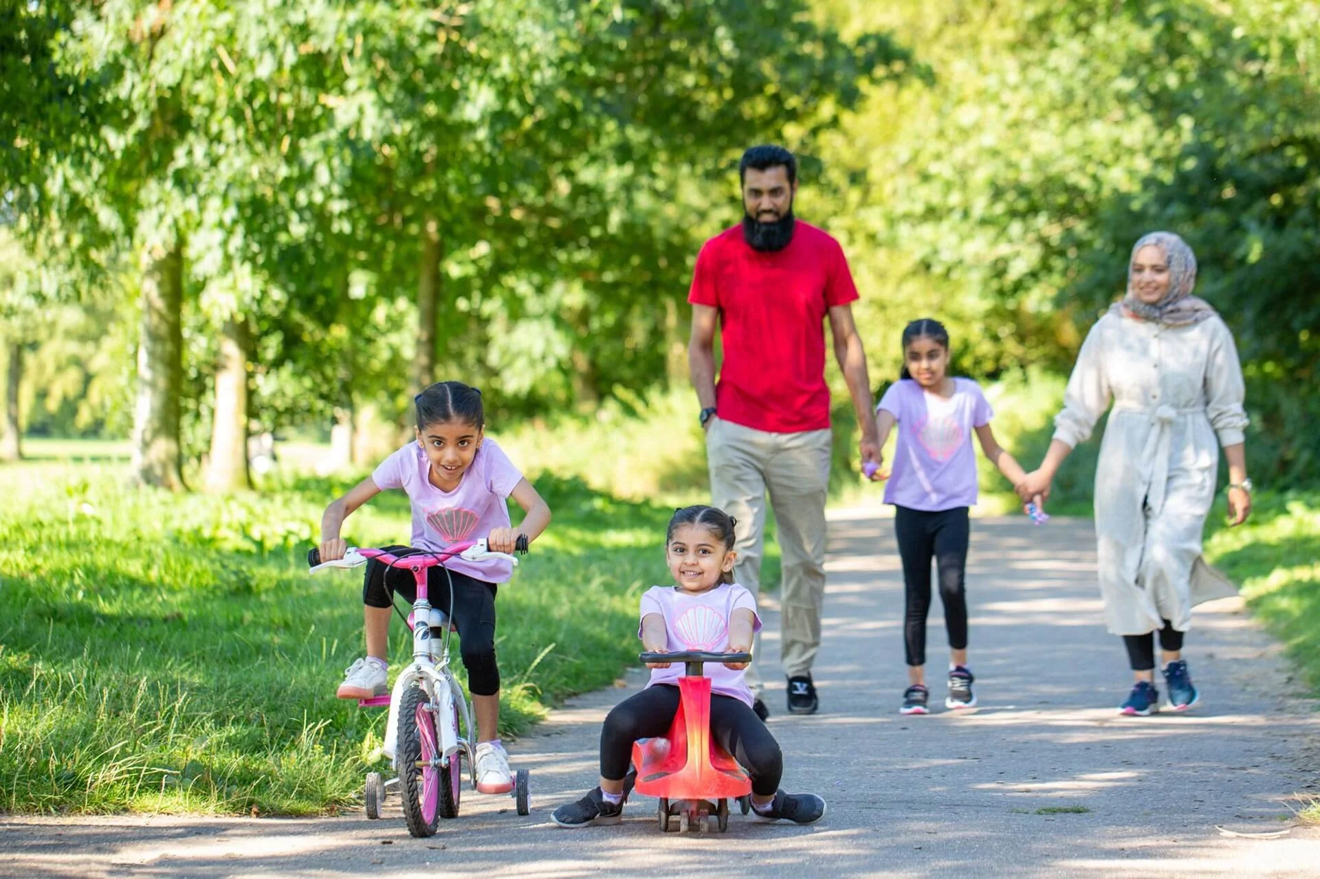 Family outdoors in a park, children riding bikes and a tricycle, with adults walking.
