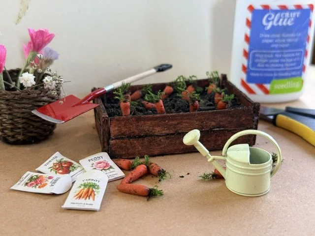 Miniature planting scene with a wooden box filled with soil and tiny carrots. Preparing a craft scene for The Wunderbox miniature gallery.