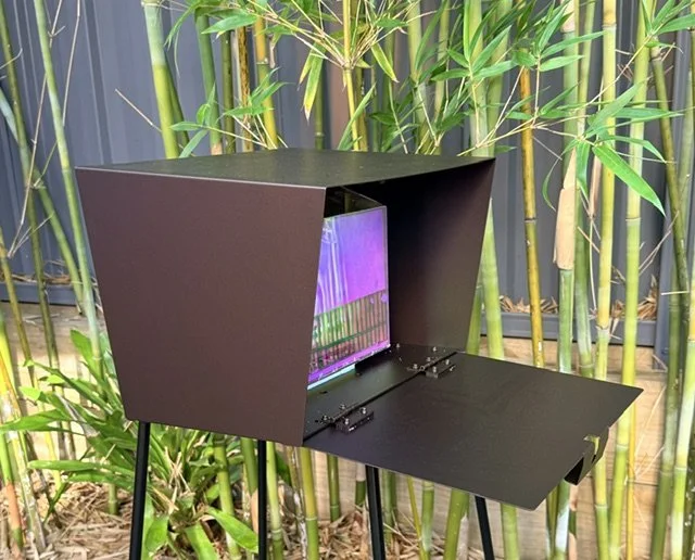 A bronze Wunderbox with door open, positioned in front of green bamboo plants.