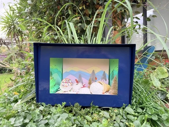 A Wunderbox diorama scene of skiers with ice cream snow, placed among green plants outdoors.