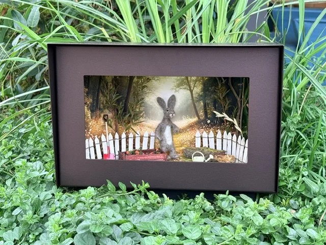 A bronze Wunderbox gallery with a felt craft rabbit, placed among green plants.