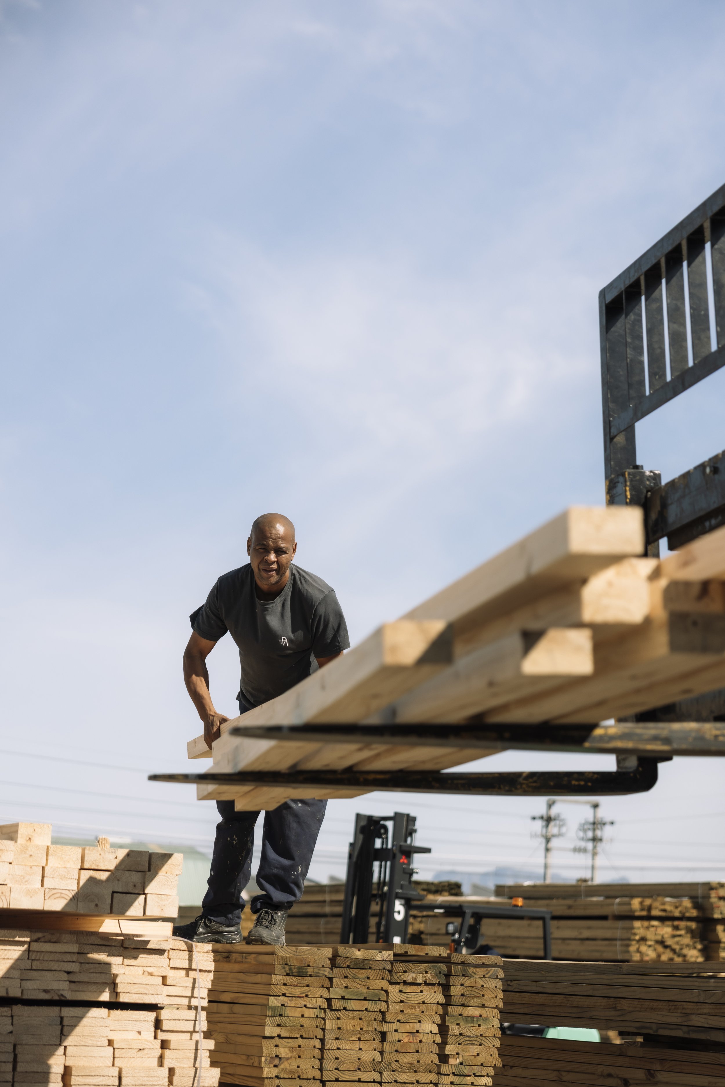 A man working on a construction site stacking wooden planks for building.