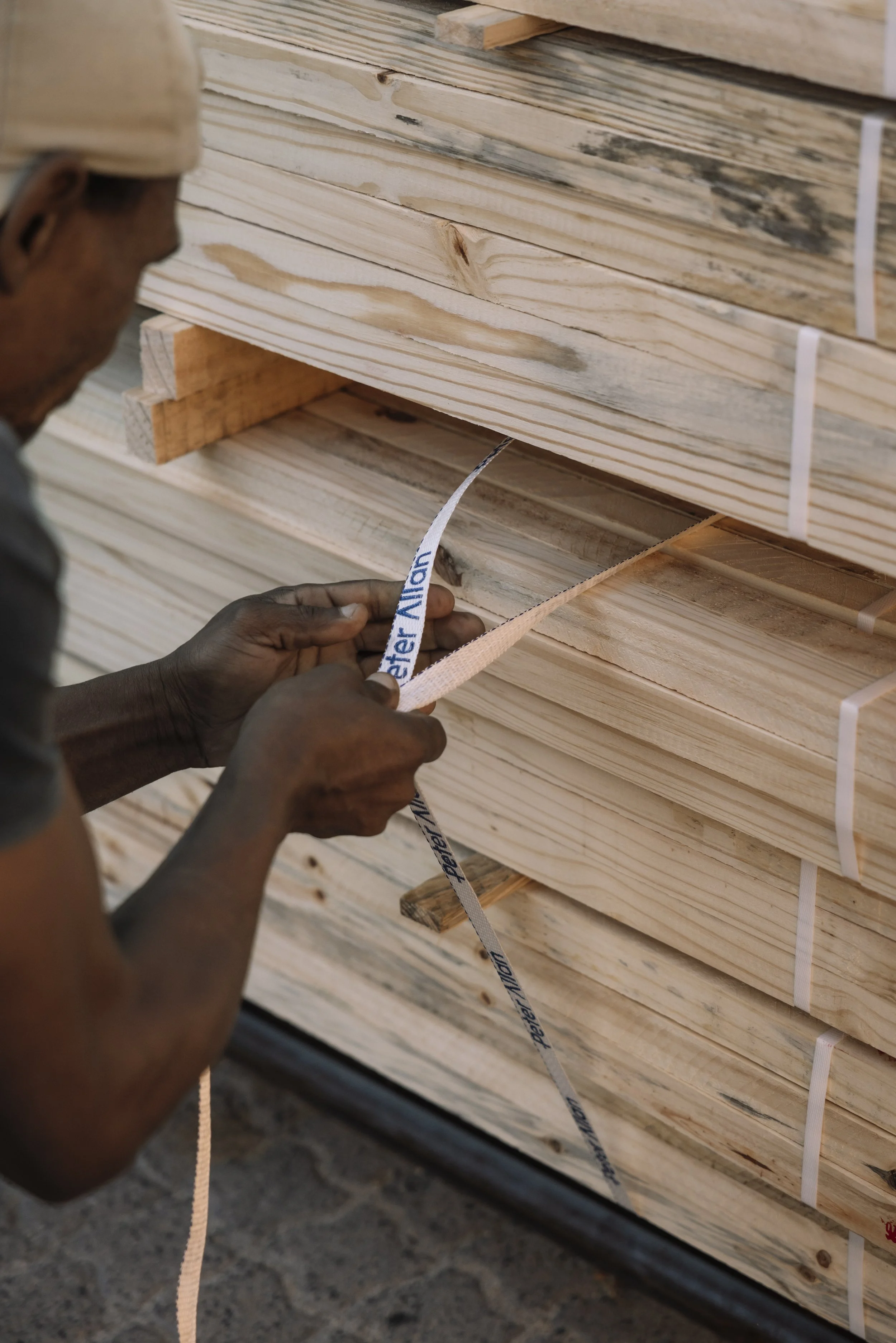 A person working with a strap on a stack of wooden planks at a lumber yard.