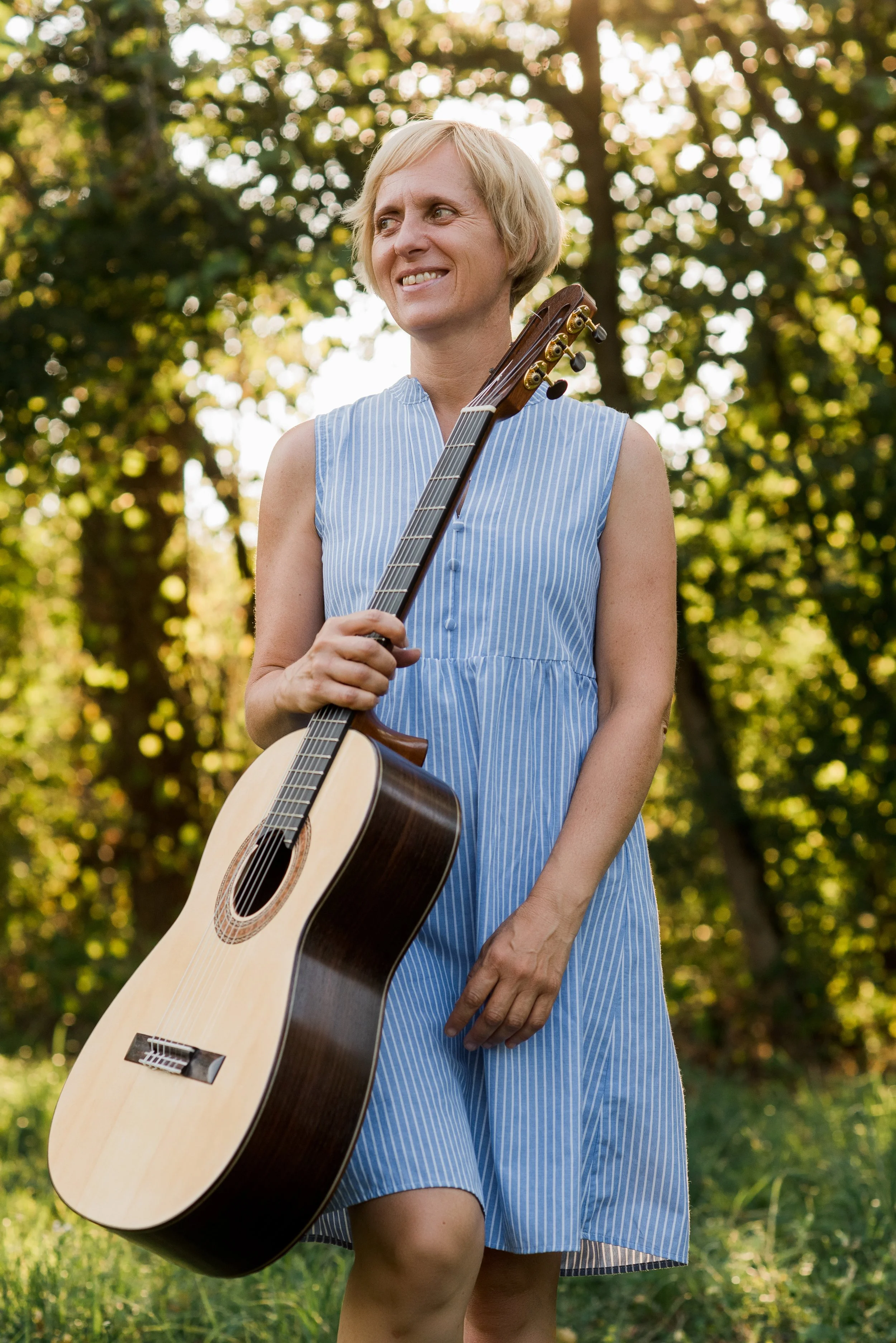 Suzuki guitar teacher Danni holding a classical guitar outdoors.