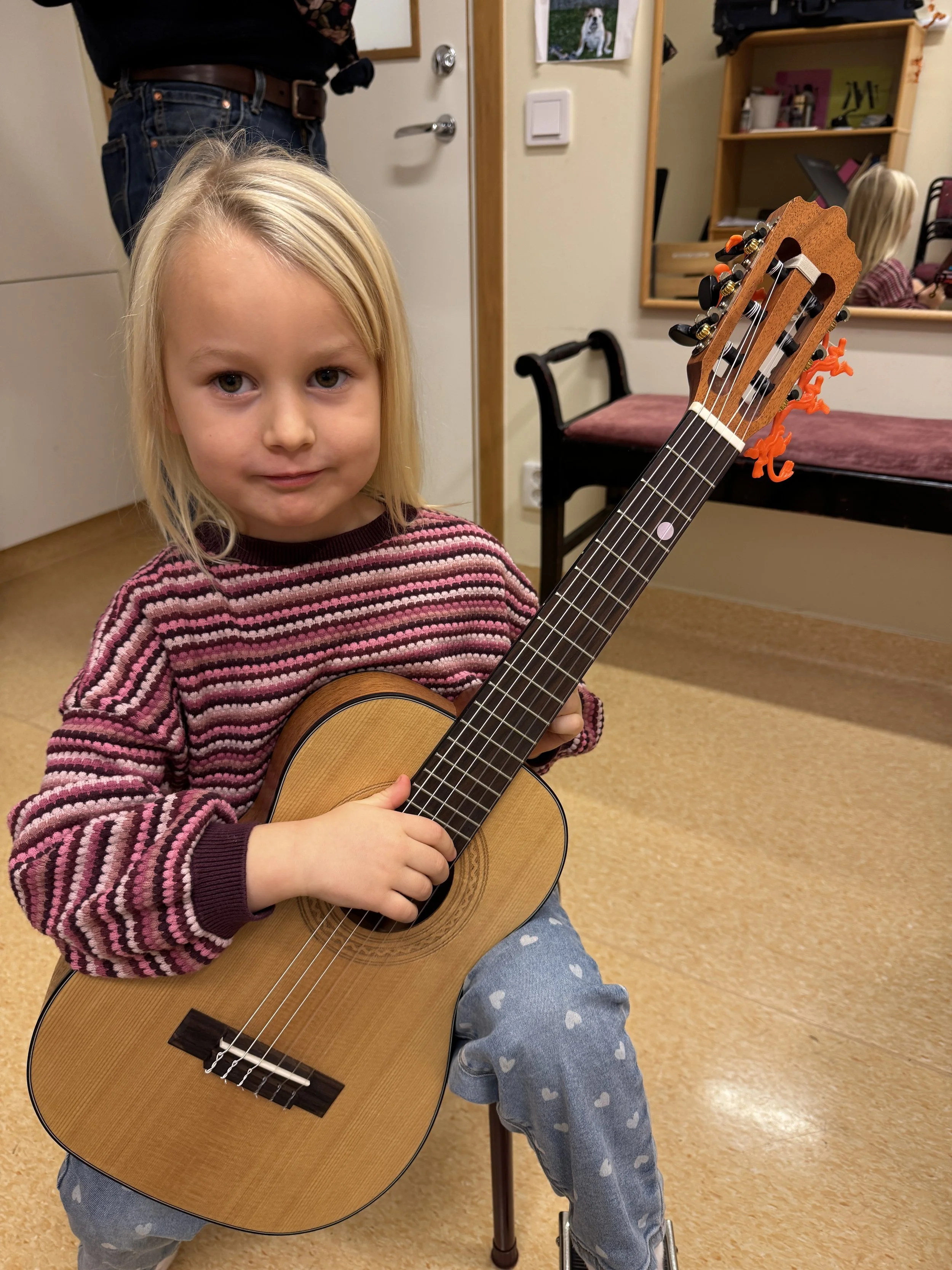 Young child playing a classical guitar during a Suzuki guitar lesson.