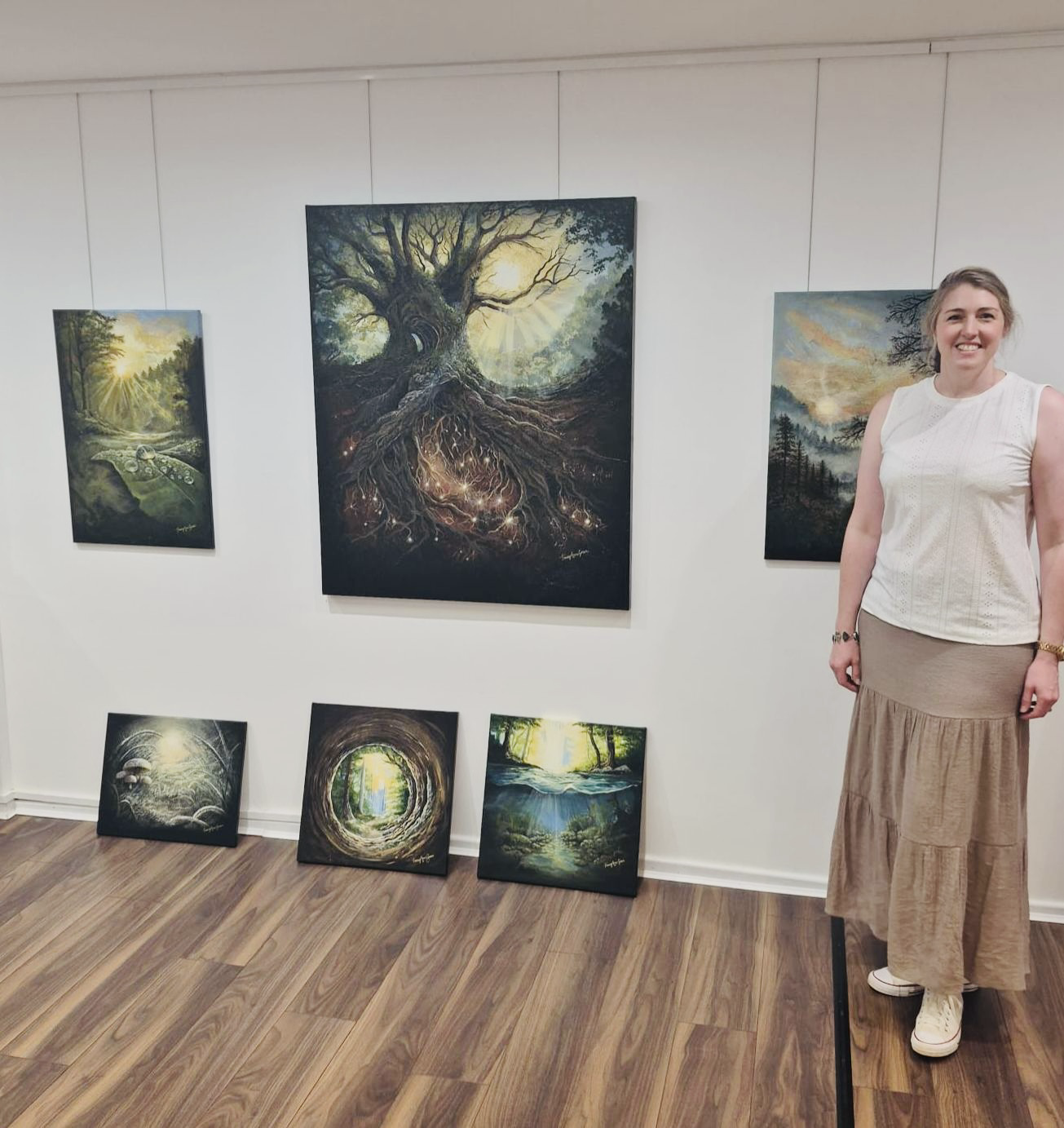 Tracey Anne Green standing beside her original nature-inspired landscape paintings at an exhibition.