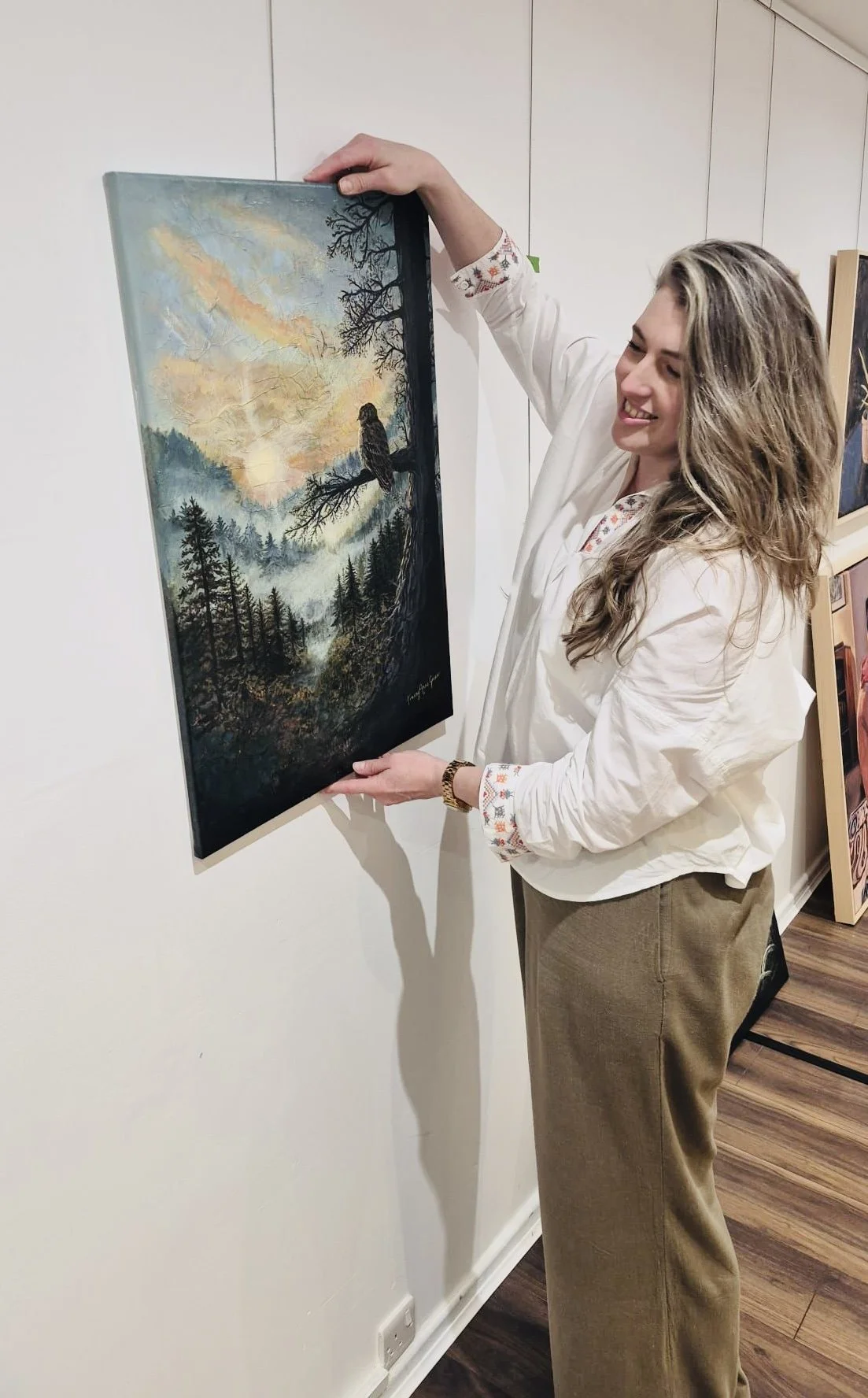 Artist Tracey Anne Green hanging her original landscape painting in a gallery, 'The Quiet Watcher'