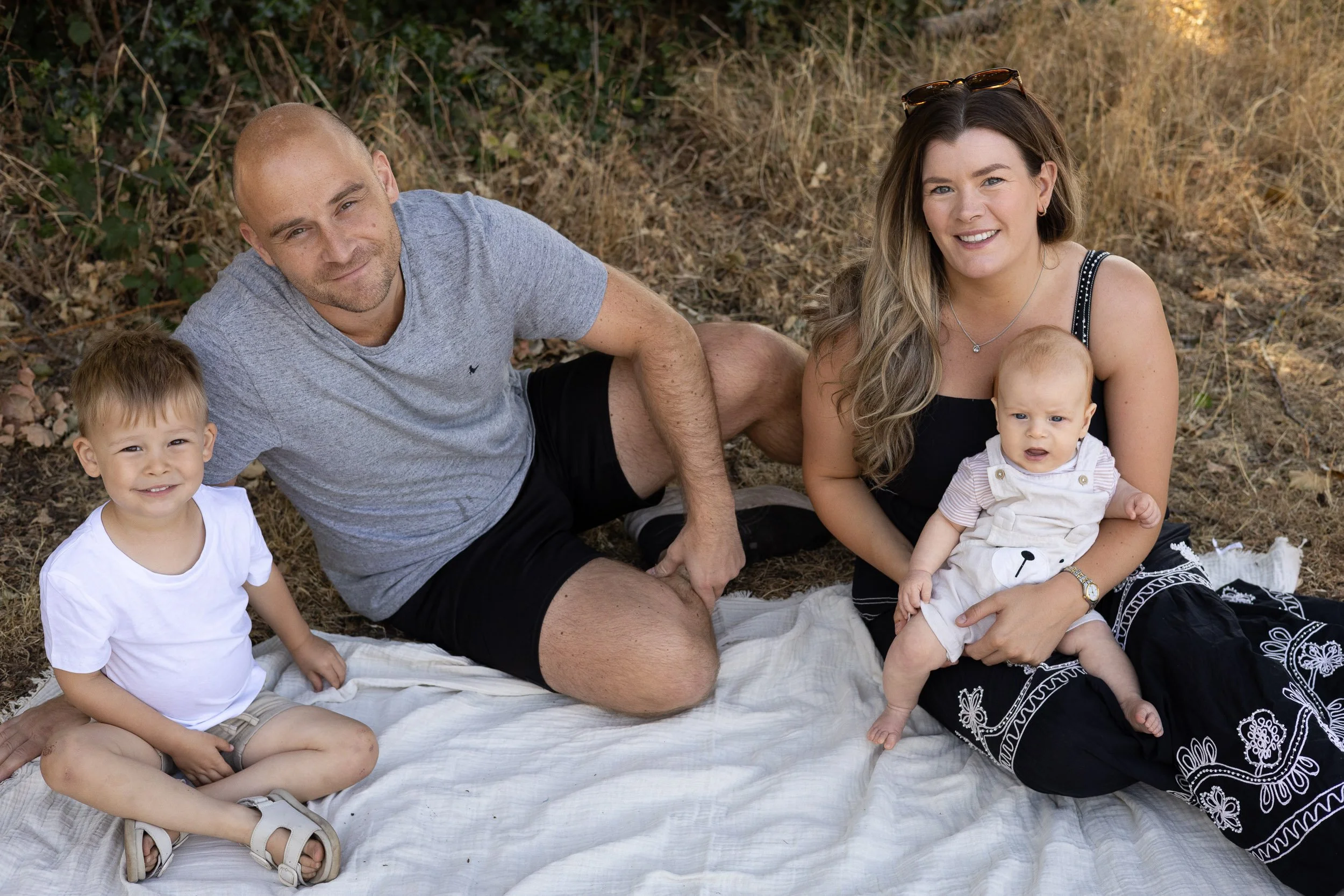 Family smiling on a picnic blanket while being photographed at Frimley Lodge Park,