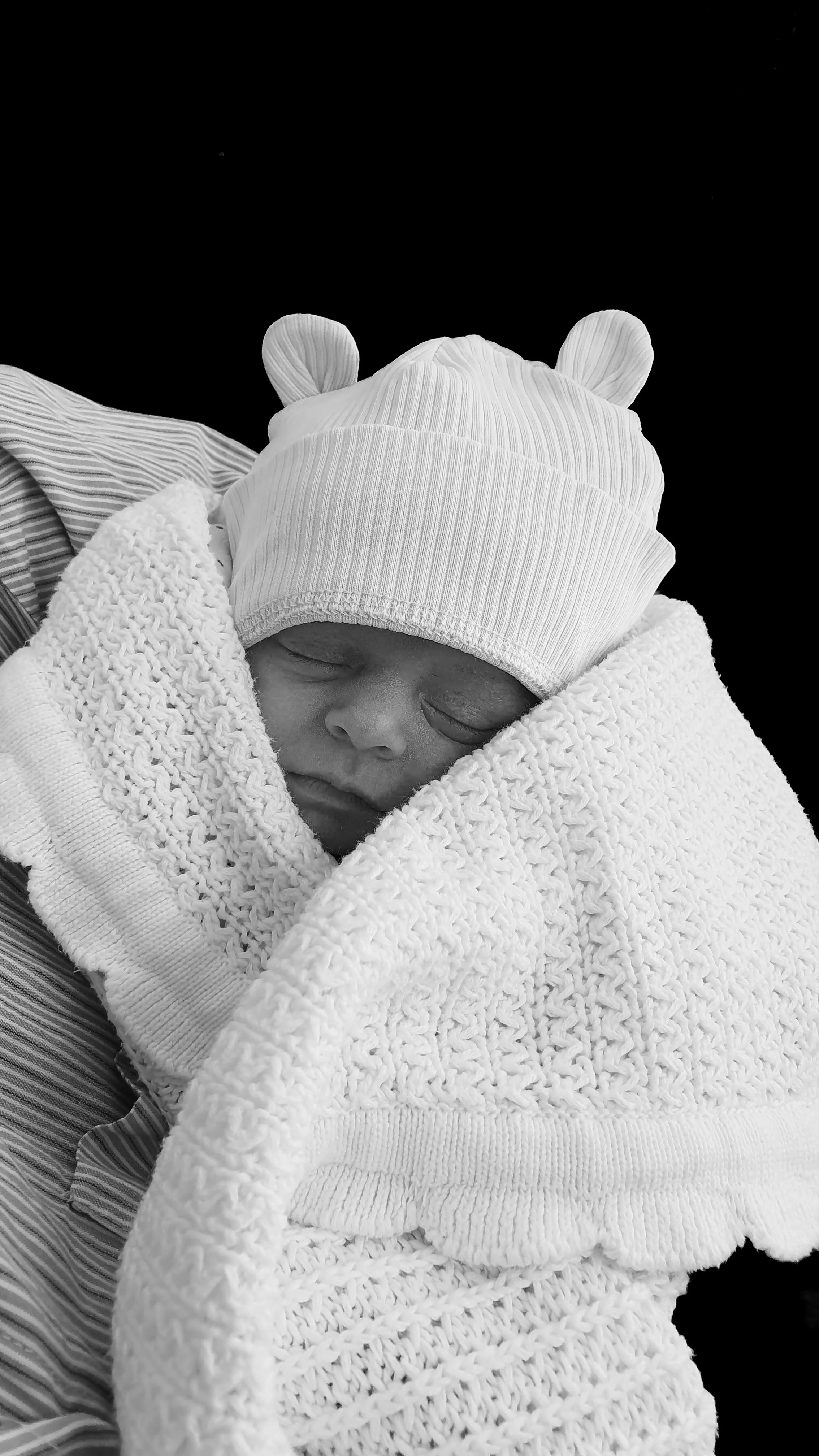 A timeless close-up of a sleeping newborn baby in a bear hat with a minimalist black background, captured in Camberley.