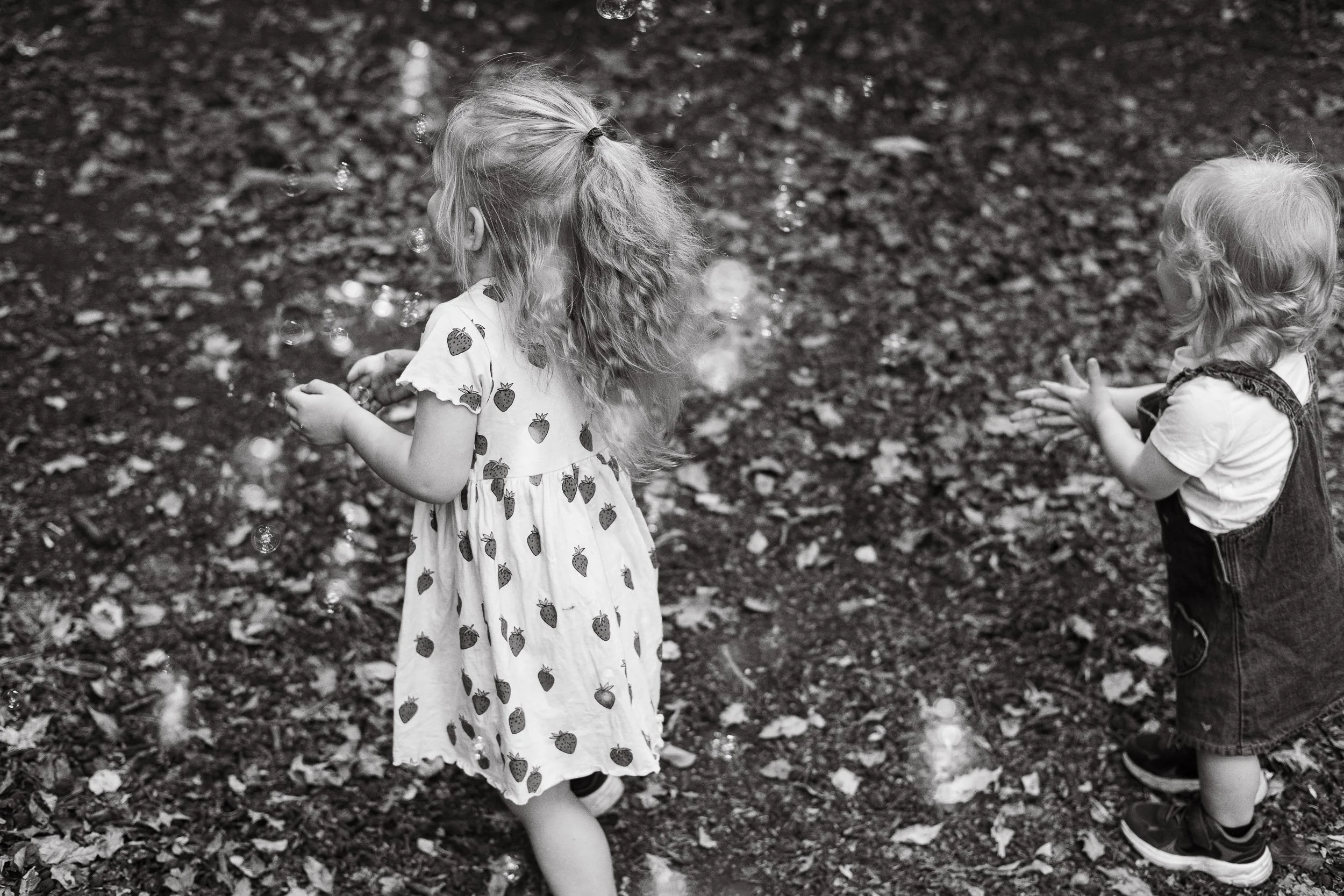 Two young toddlers playing with bubbles during a candid outdoor family photography session in Farnborough